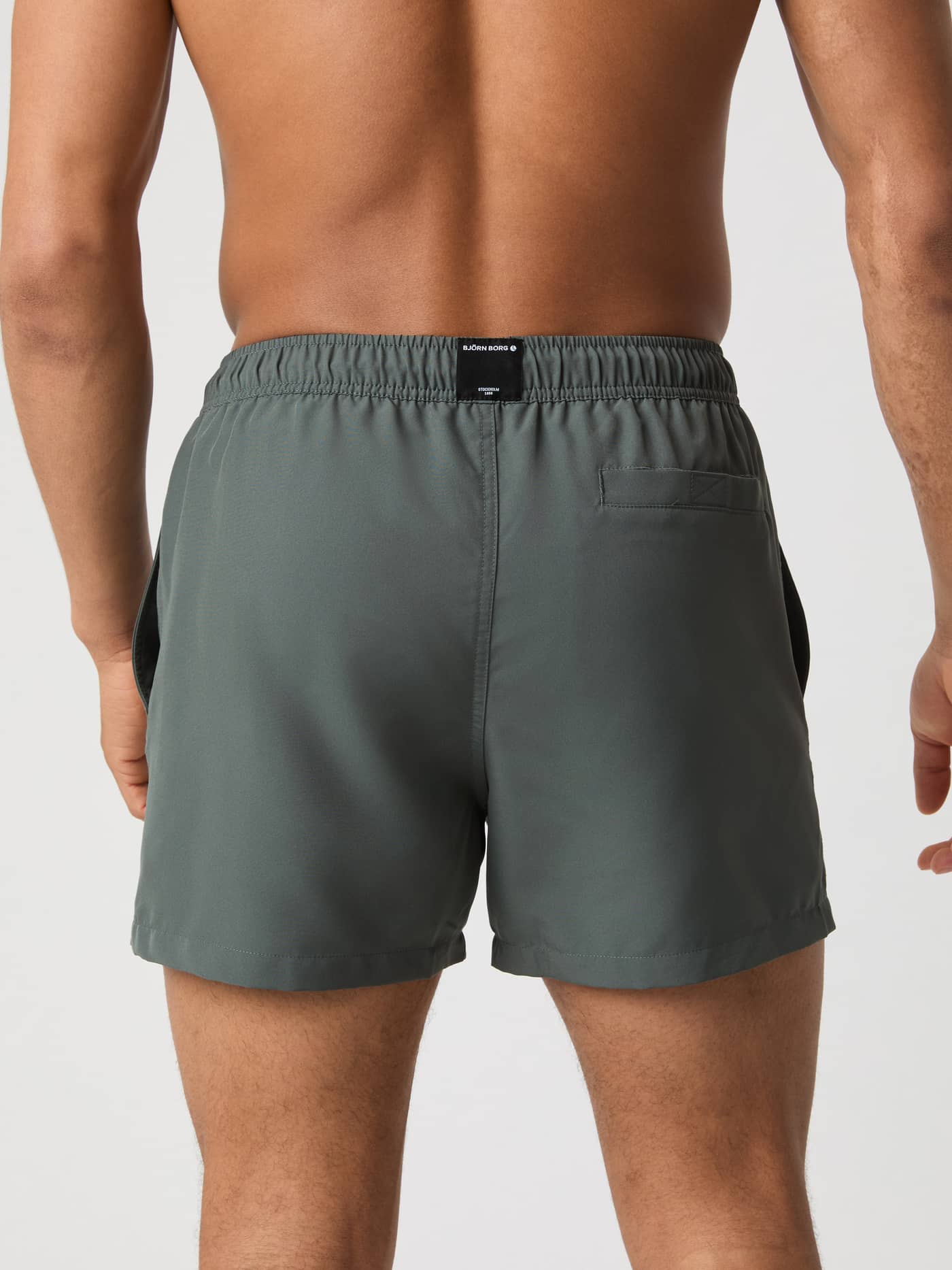 Back view of a man wearing Björn Borg Solid Swim Shorts in Urban Chic (Green), made of recycled polyester with a black logo. - Image 3