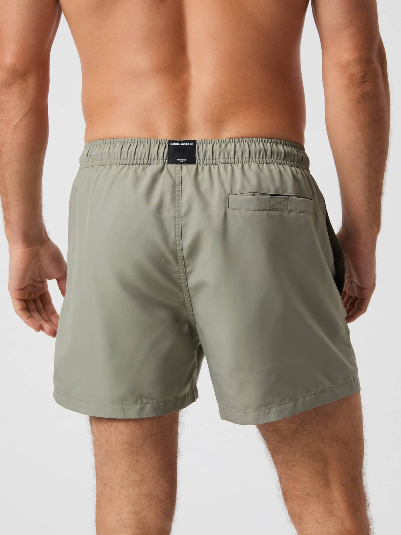 Vista trasera de un hombre con Borg Solid Swim Shorts en Vetiver (Verde) y etiqueta de logotipo negra en la cintura. - Image 3