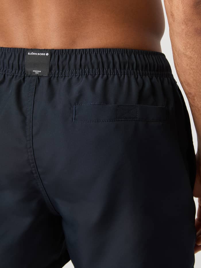 Achteraanzicht van de Borg Solid Swim Shorts in Night sky (Marineblauw) met een functionele klittenbandzak en wit logo. - Image 4