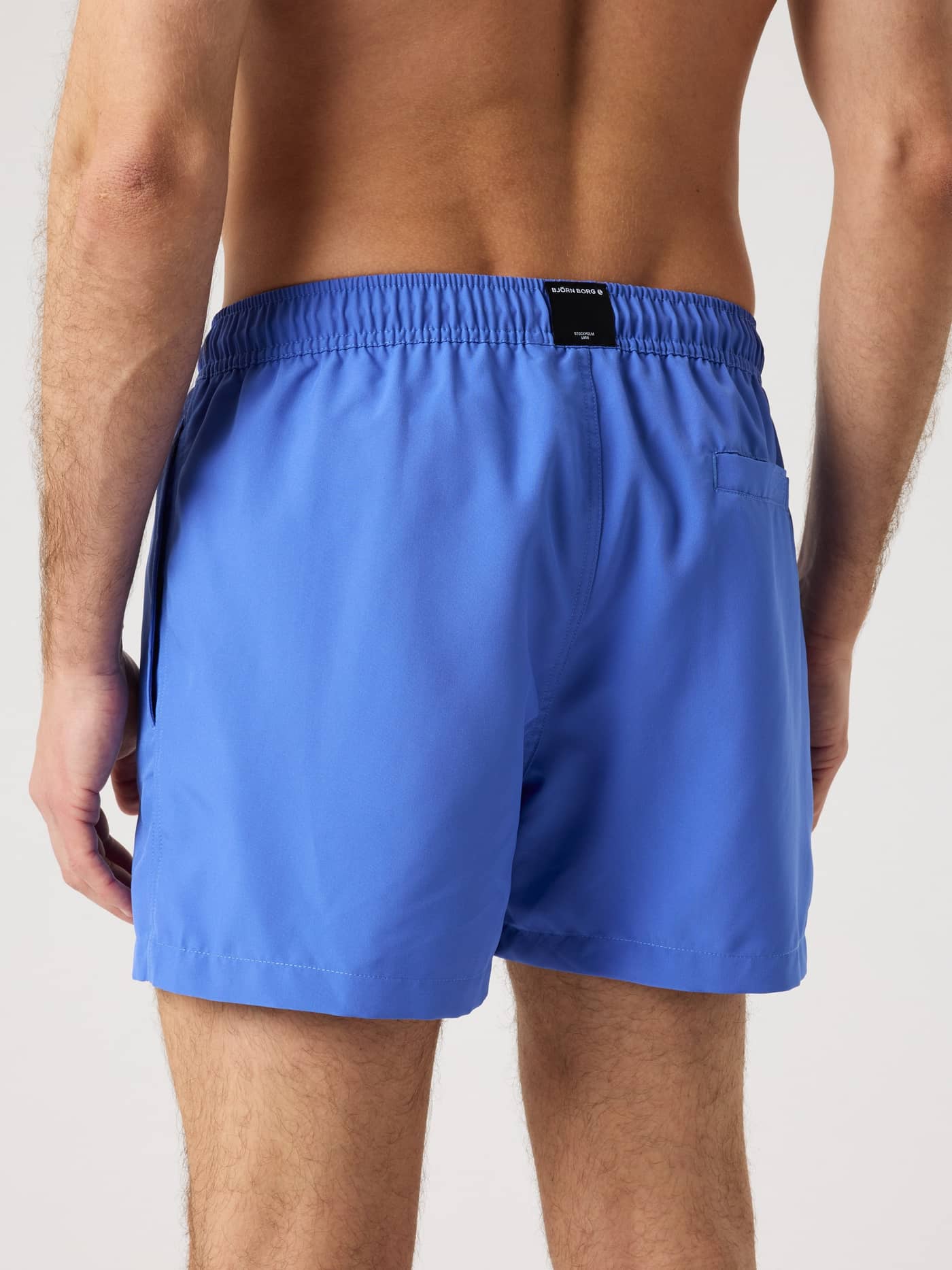 Back view of a man wearing blue Borg Solid Swim Shorts made from recycled material with a functional back pocket. - Image 2