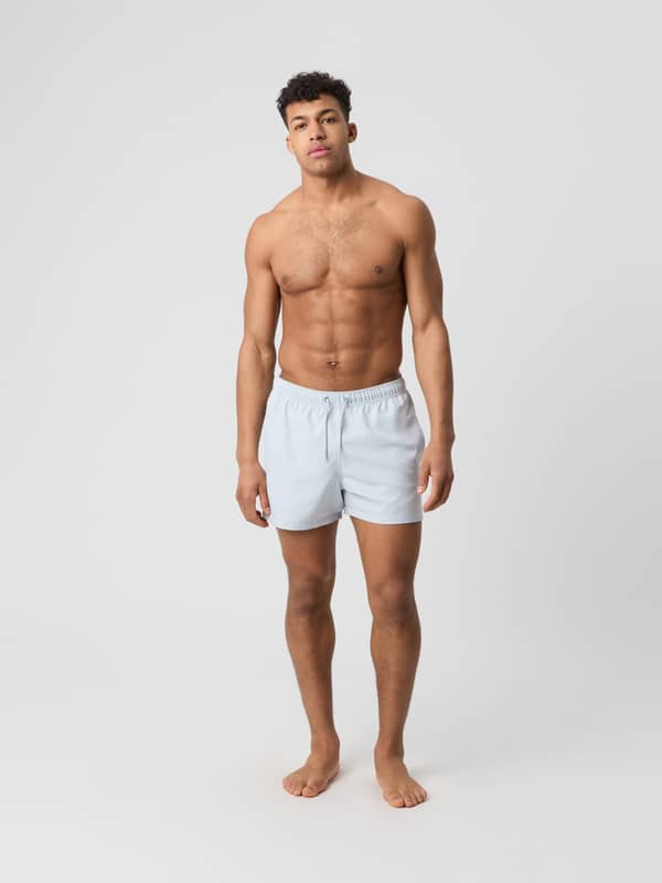 Mand set forfra i fuld figur iført de løstsiddende Borg Solid Swim Shorts i Gray Dawn (Grå) af genbrugspolyester.