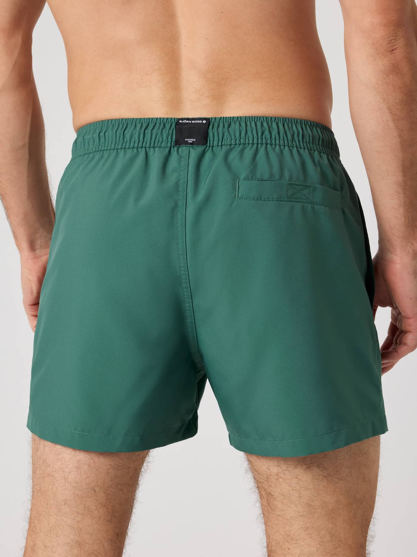 Back view of a man wearing Mallard Green (Green) Borg Solid Swim Shorts, featuring a loose fit and functional back pocket. - Image 2