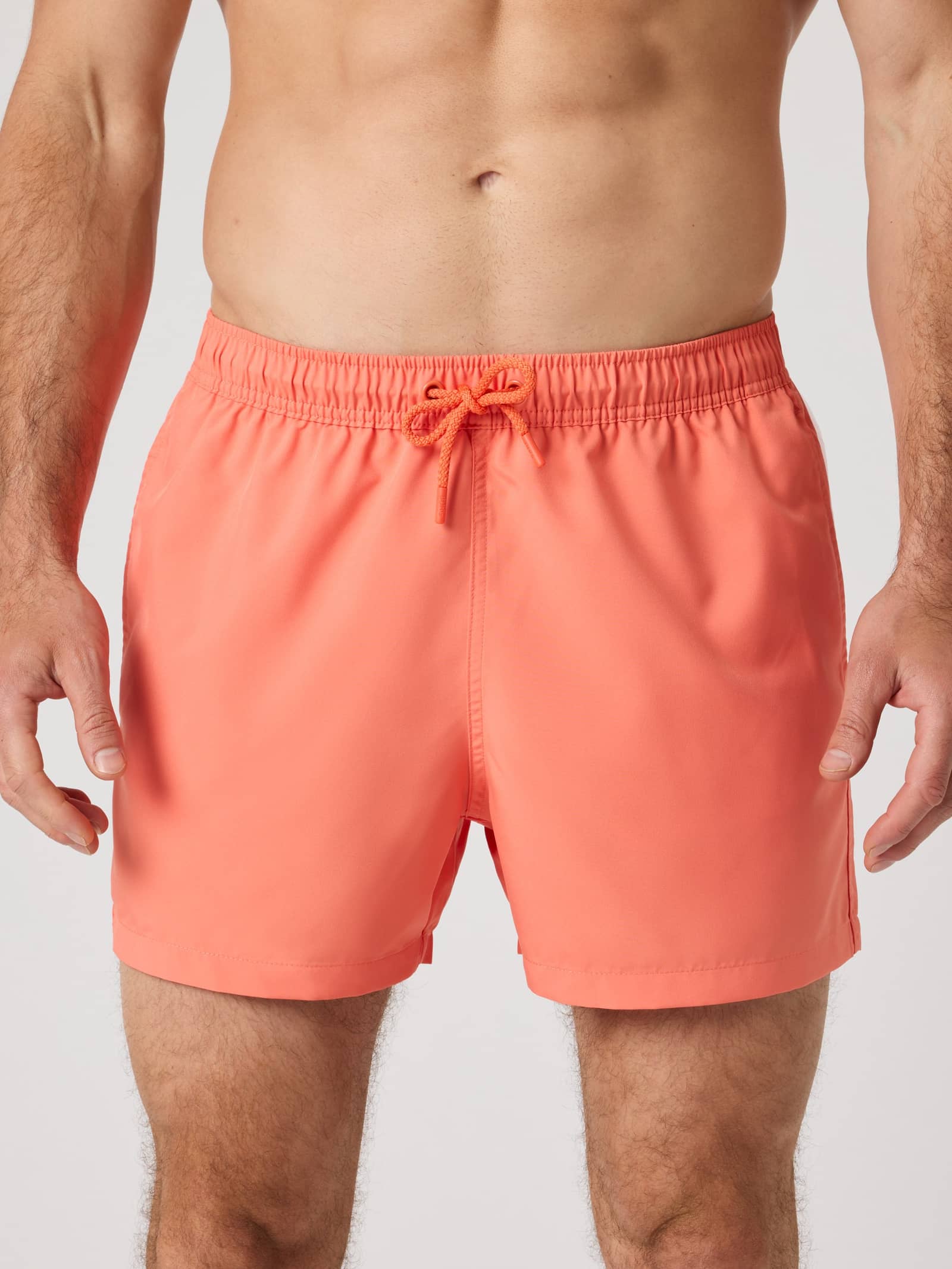 Borg Solid Swim Shorts i Coral (Orange) i återvunnen polyester med lös passform sedda framifrån på en man. - Image 1