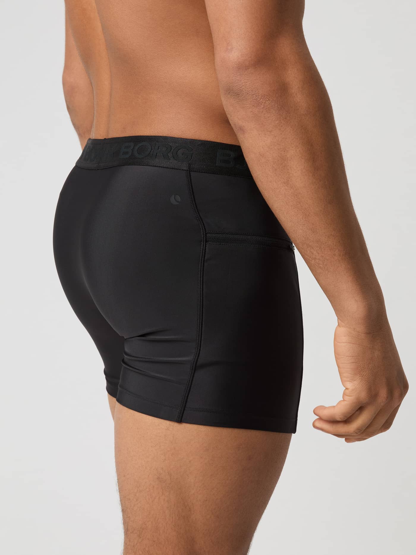Side view of a man wearing Björn Borg Stretch Swim Shorts in Black Beauty (Black) with a zippered pocket and tennis detail. - Image 3
