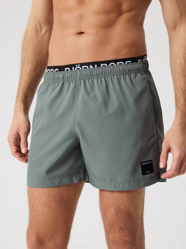 Borg Elastic Swim Shorts i Balsam Green (Grøn) set forfra på en mand med en sort elastisk linning med hvidt logo.