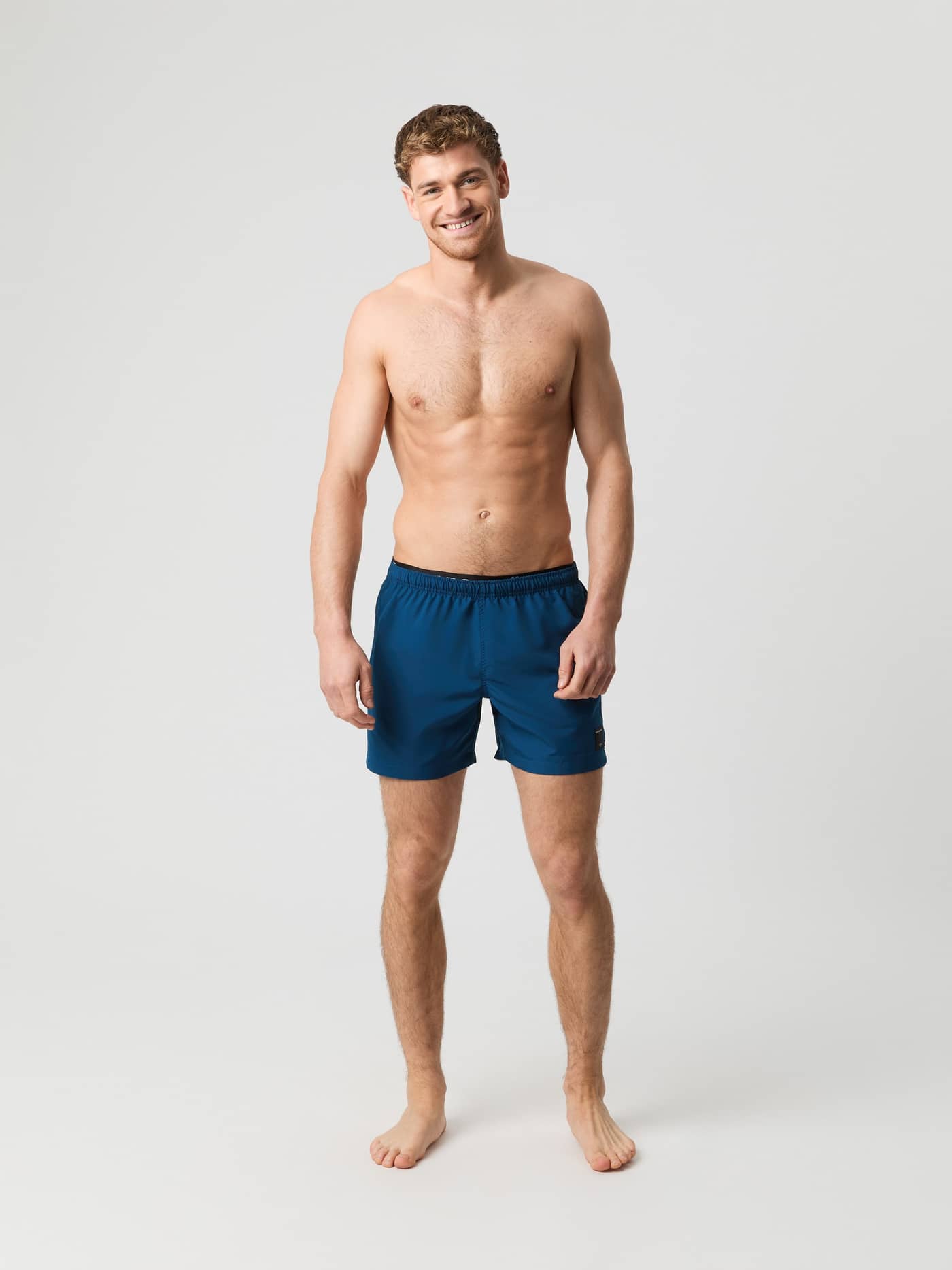 Full-body front view of a man in functional Borg Elastic Swim Shorts in Gibraltar Sea (Blue) made from recycled polyester. - Image 1