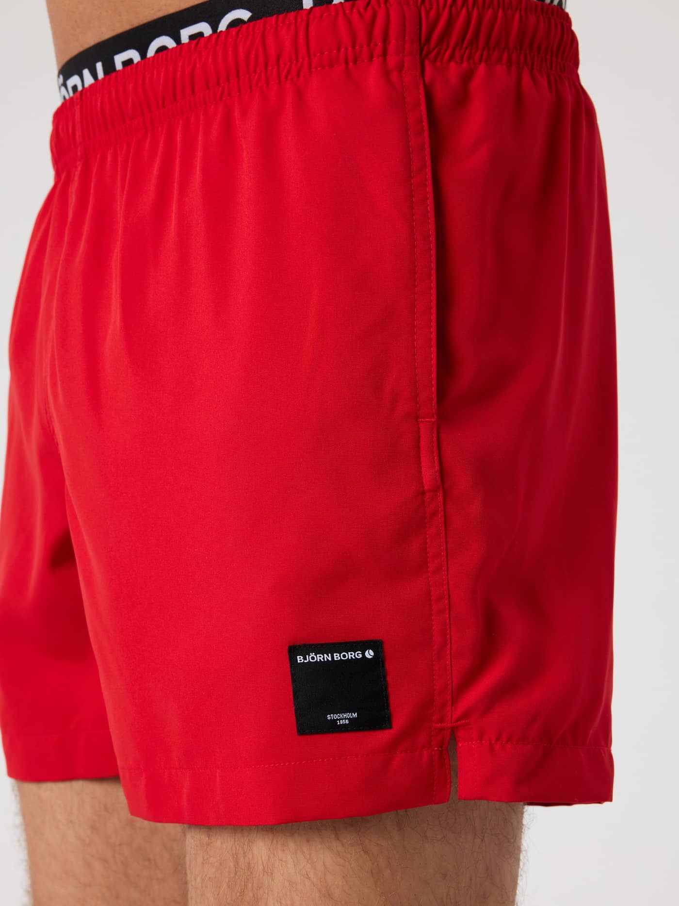 Side view of the red Borg Elastic Swim Shorts, highlighting the black woven logo label and branded elastic waistband. - Image 5