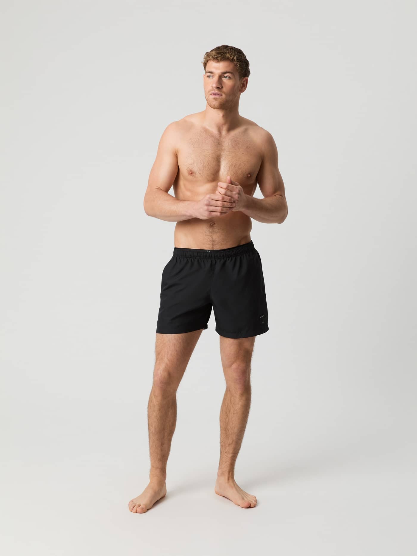 Full-body front view of a man wearing Björn Borg Elastic Swim Shorts in Black Beauty (Black), made from recycled polyester. - Image 1