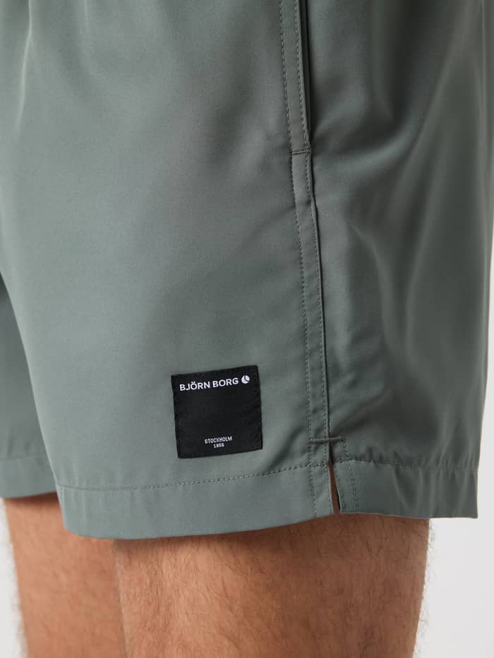 Close-up van de zwarte logopatch op de pijp van de Balsam Green (Groen) Borg Elastic Swim Shorts. - Image 5