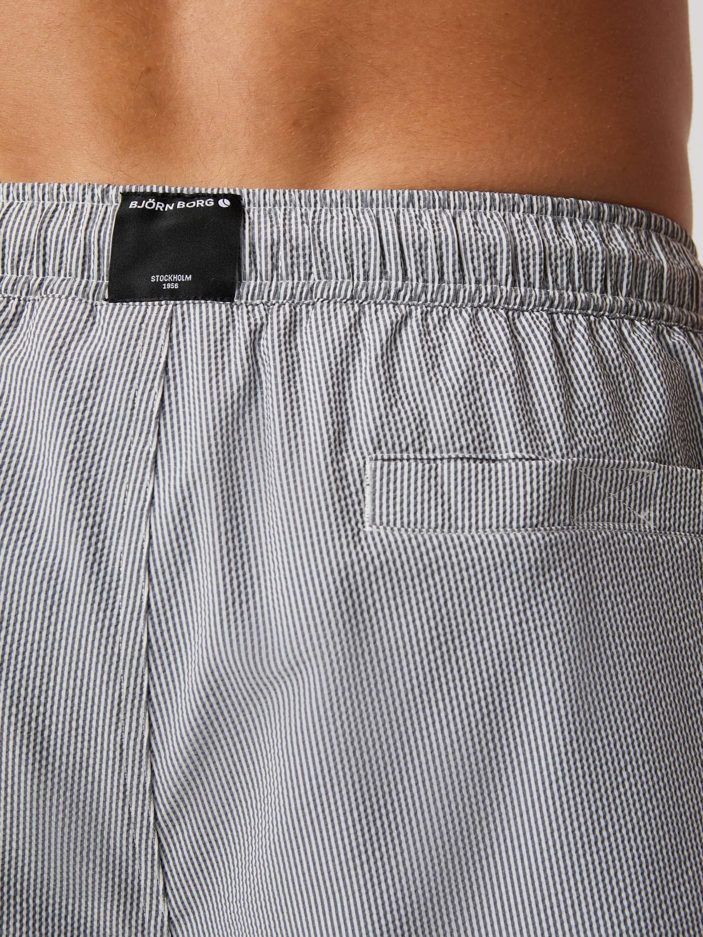 Back detail of the striped Borg Seersucker Swim Shorts in Swim Stripe 4 (Grey) with a Velcro pocket and black logo label. - Image 4