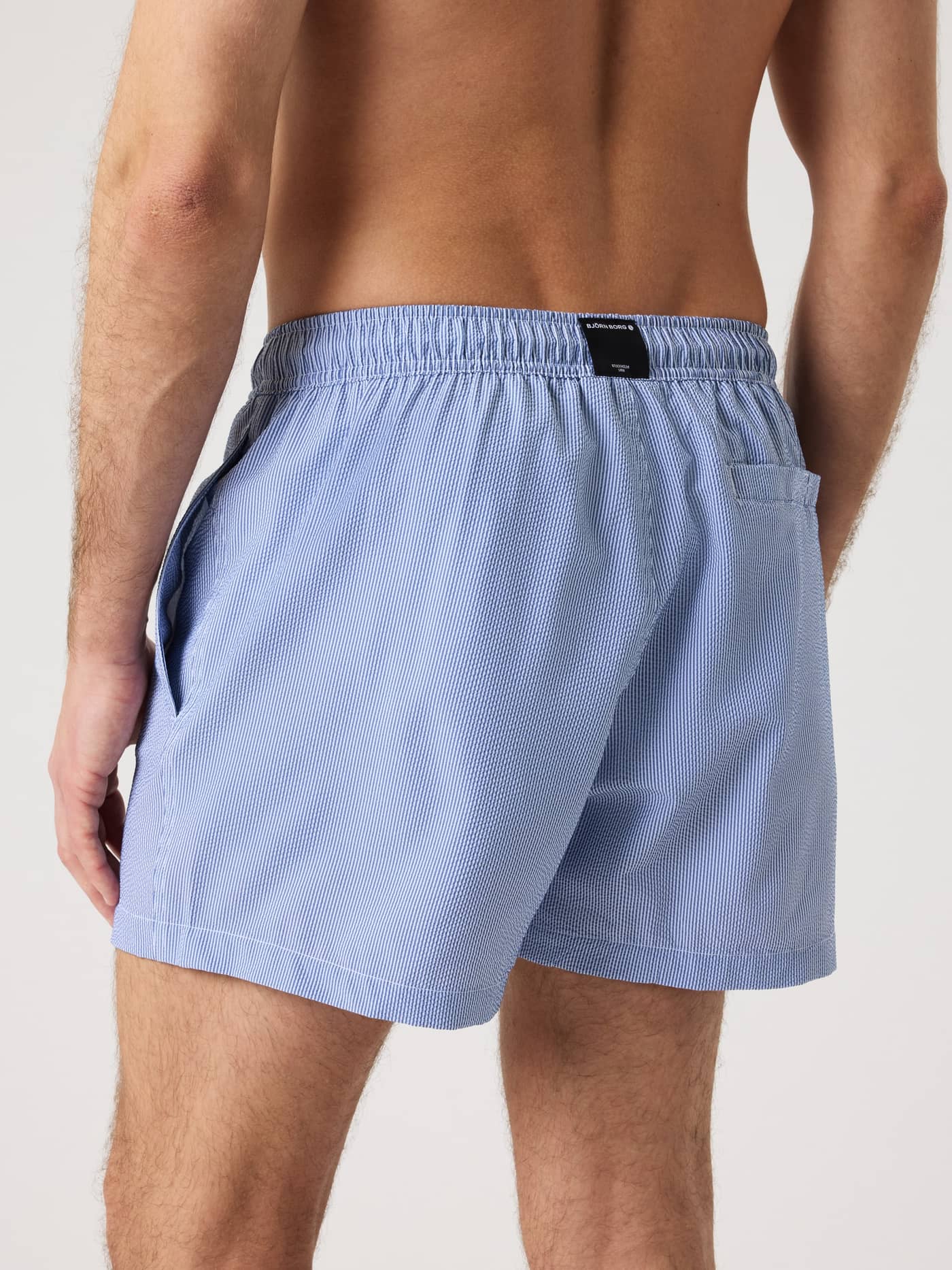 Back view of a man wearing the Borg Seersucker Swim Shorts in Blue with a striped pattern and black logo. - Image 2
