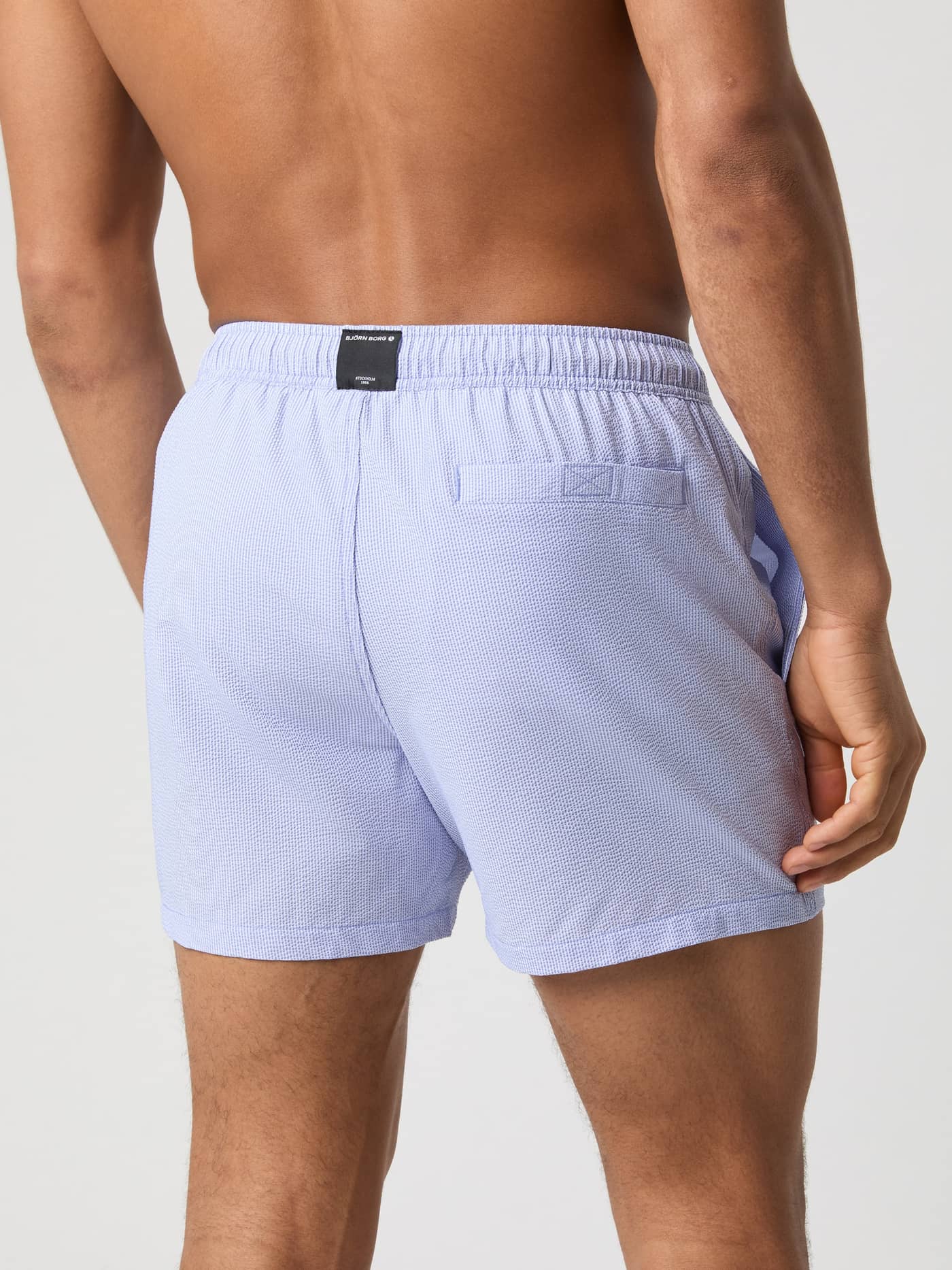 Vista posterior de hombre con Borg Seersucker Swim Shorts en Swim Stripe 2 (Azul) a rayas y logotipo negro. - Image 3