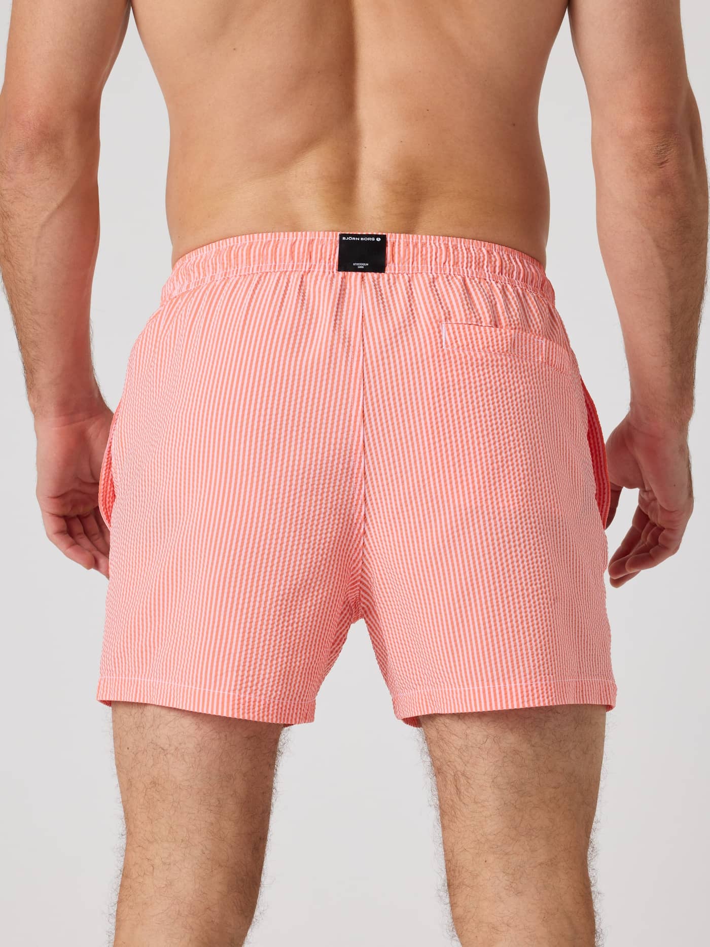 Back view of a man wearing the striped Borg Seersucker Swim Shorts in Searstripe 6 (Red) featuring a black waistband logo. - Image 2