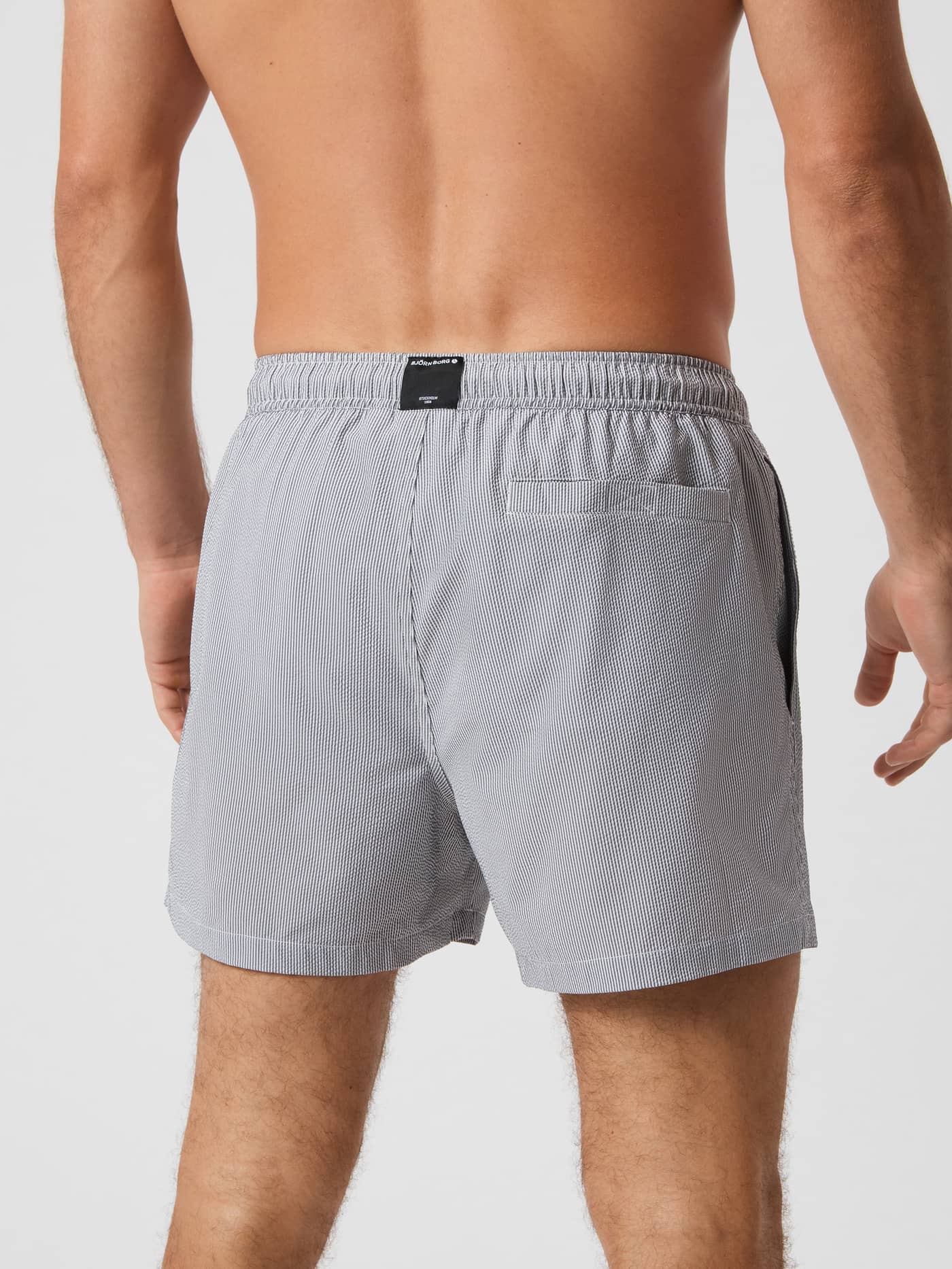 Back view of a model wearing the striped Borg Seersucker Swim Shorts in Swim Stripe 4 (Grey) featuring a back pocket. - Image 3