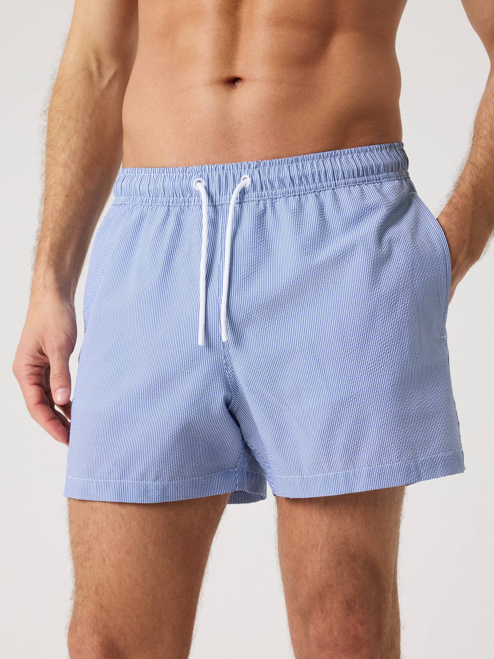 Front view of a man wearing the blue Borg Seersucker Swim Shorts featuring a striped pattern and white drawstring. - Image 1