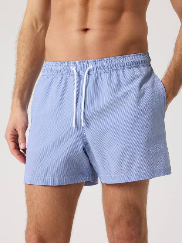 Front view of a man wearing the blue Borg Seersucker Swim Shorts featuring a striped pattern and white drawstring.