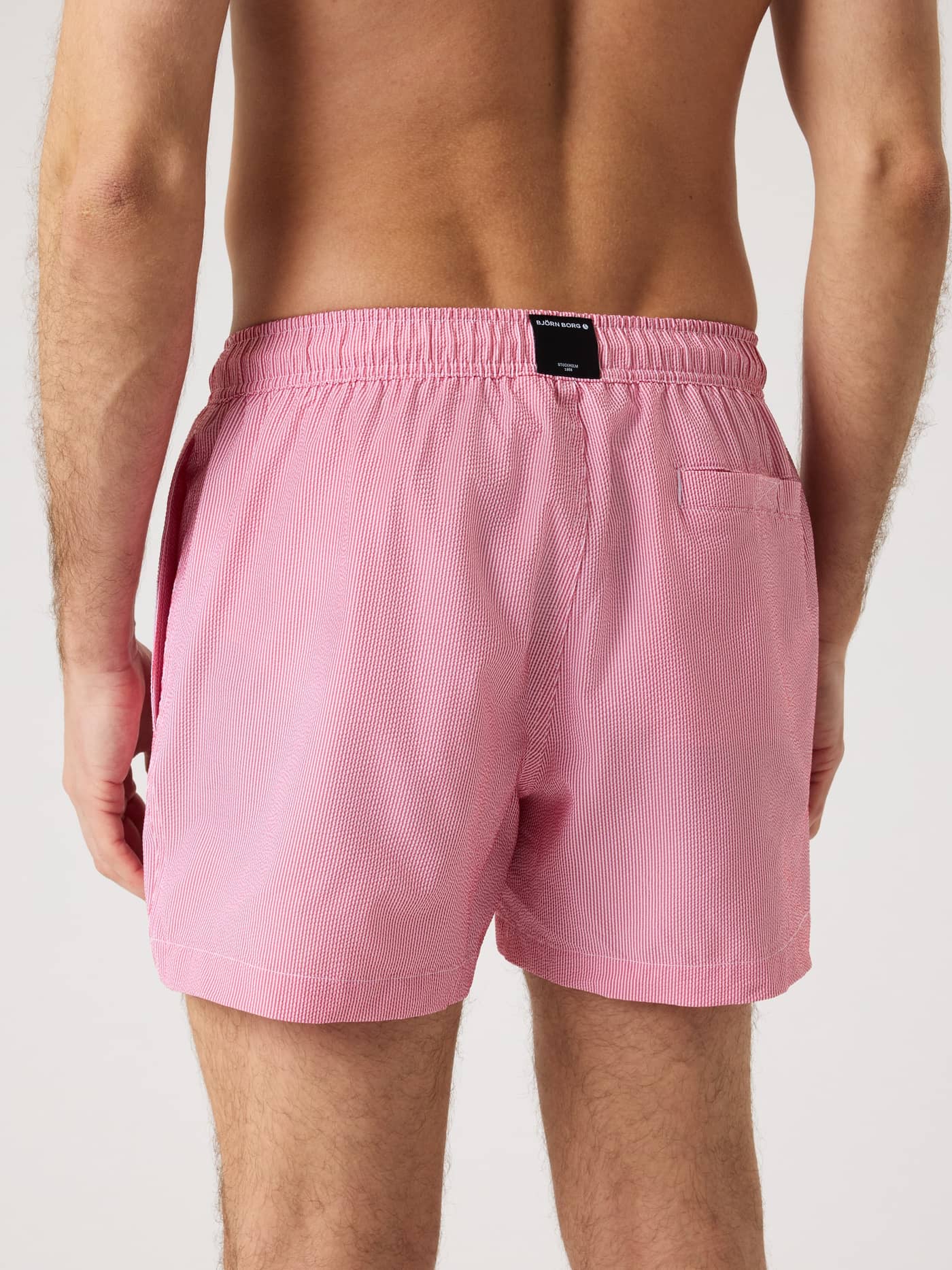 Vista trasera de los Borg Seersucker Swim Shorts en Searstripe 3 (Rojo) con rayas, etiqueta negra y bolsillo trasero. - Image 2