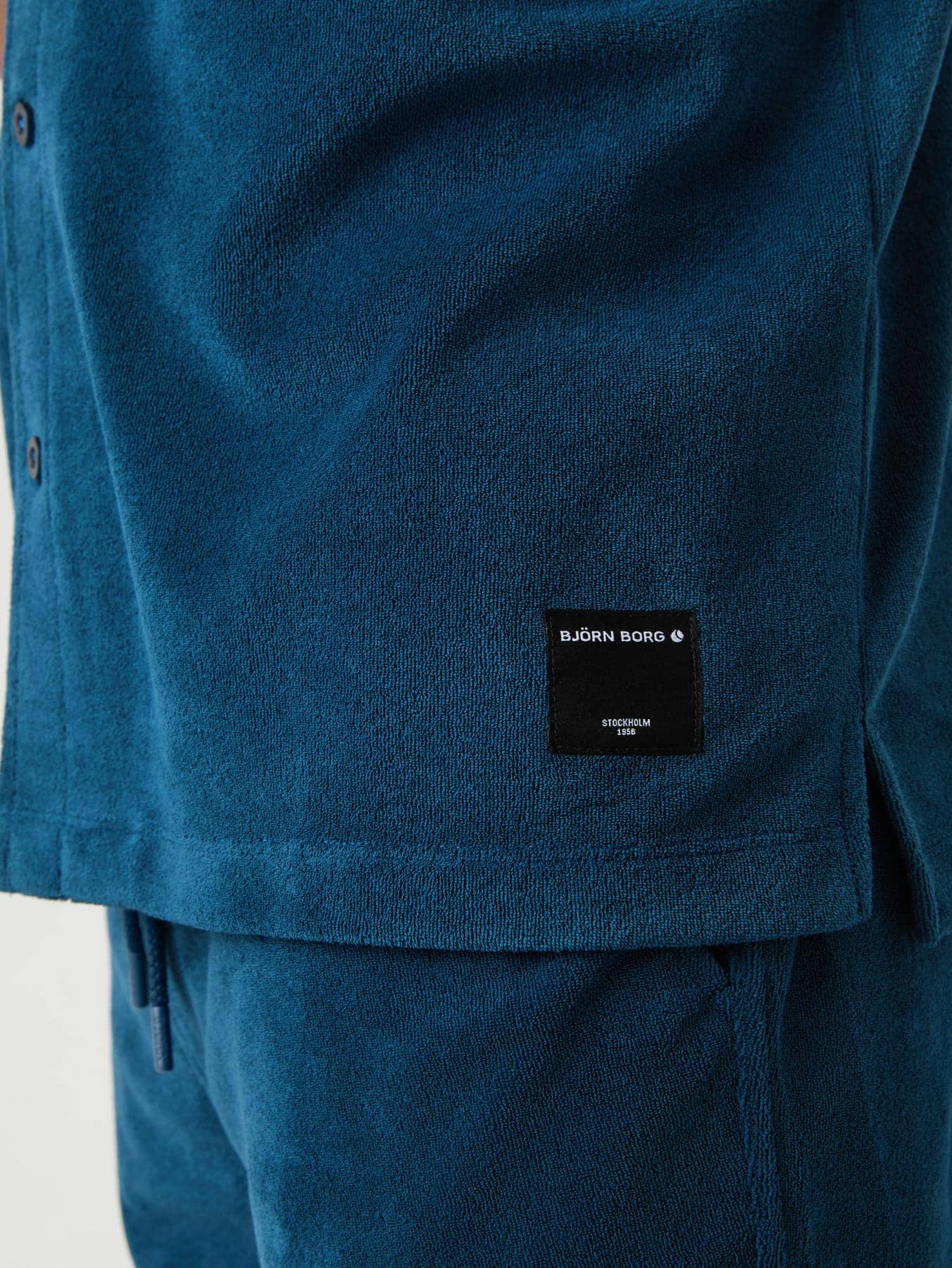 Close-up of the Gibraltar Sea (Blue) Borg Toweling Pool Shirt highlighting the toweling fabric and black logo label. - Image 5