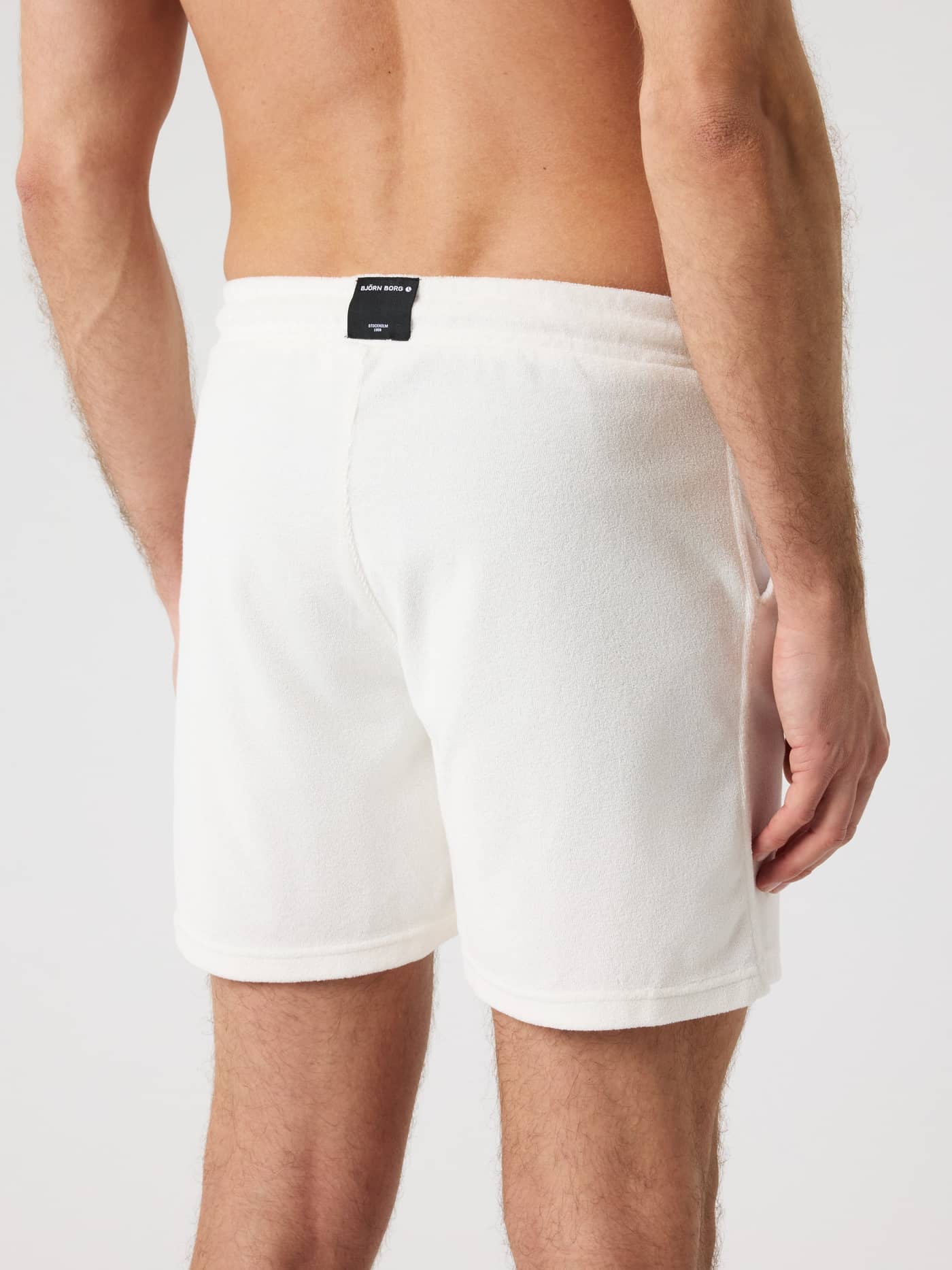 Vista posterior de un hombre con Borg Toweling Pool Shorts en Tofu (Blanco) de rizo suave y etiqueta de logo negra. - Image 2