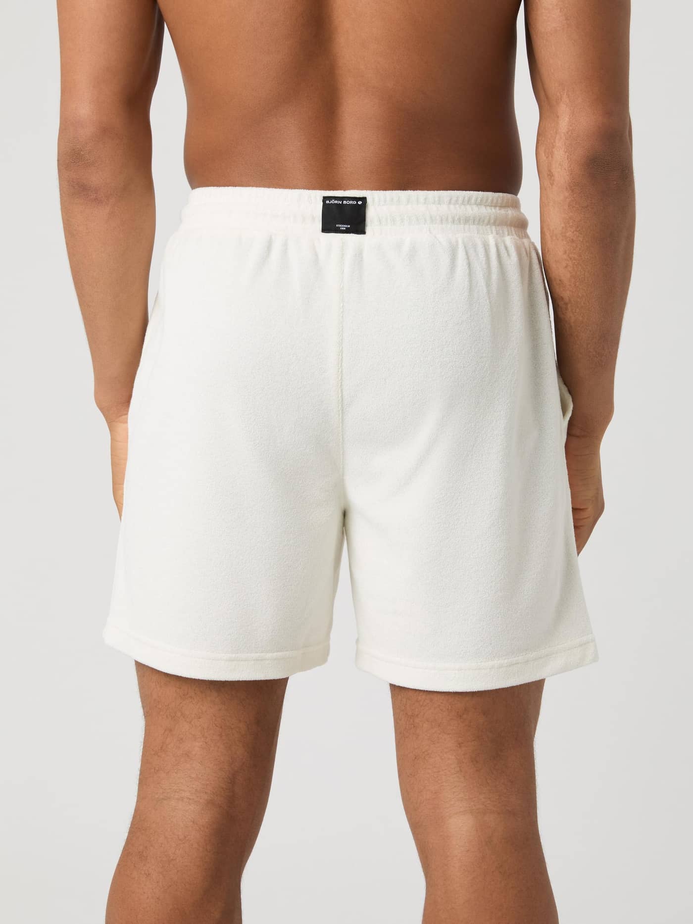 Back view of a man wearing the Borg Toweling Pool Shorts in Egret (White) in soft toweling fabric with a black logo label. - Image 3