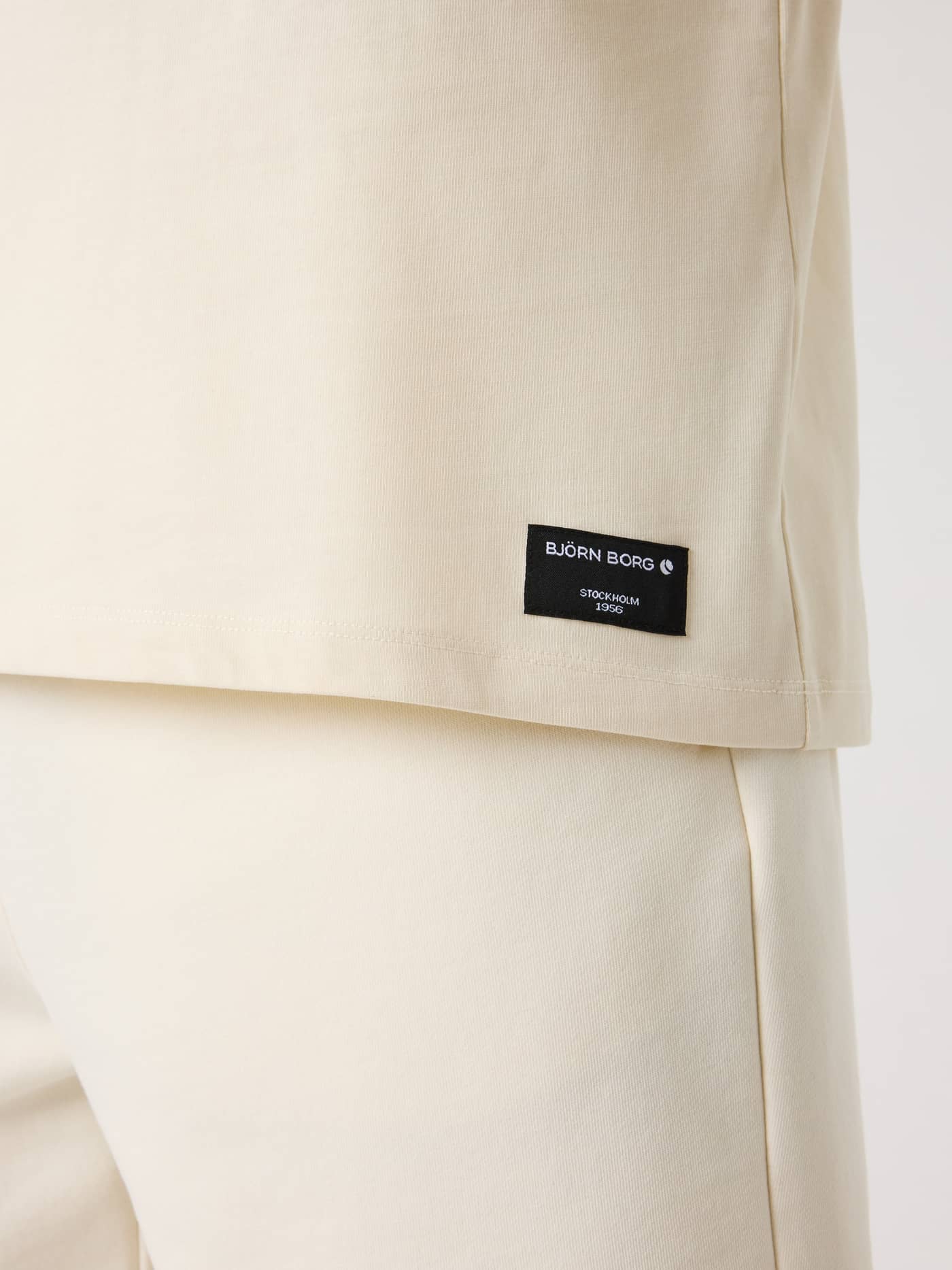 Nahaufnahme des schwarzen Logo-Labels am Centre High Neck T-Shirt für Herren in Tofu (Weiß) aus weicher Baumwolle. - Image 4