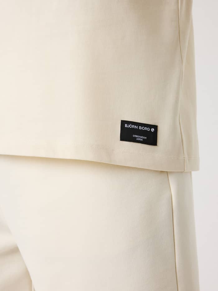 Close-up of the black logo label on the cotton Tofu (White) Centre High Neck T-Shirt for men.
