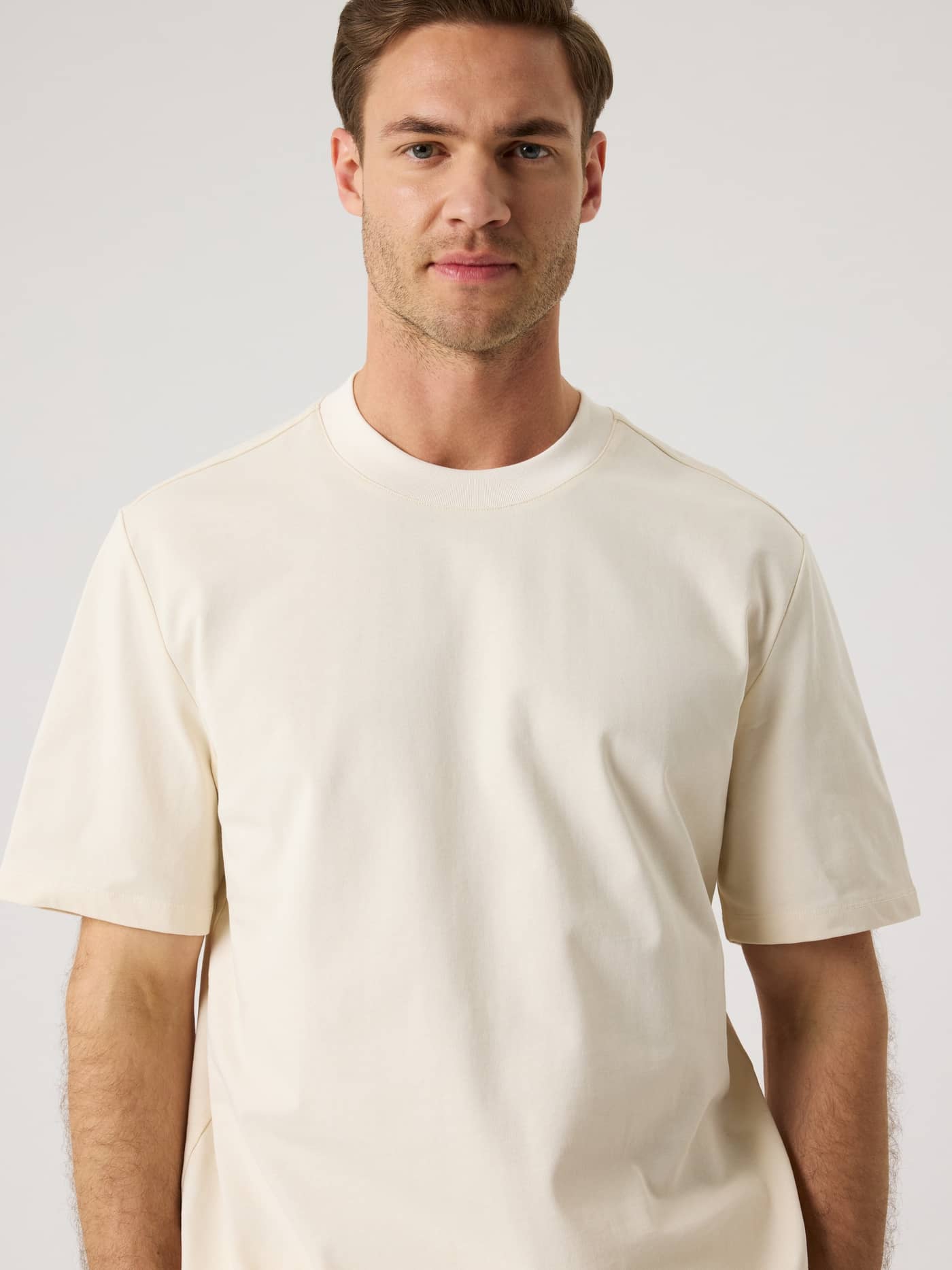 Vorderansicht eines Mannes im Centre High Neck T-Shirt in Tofu (Weiß) aus weicher Baumwolle mit Oversized-Passform. - Image 5