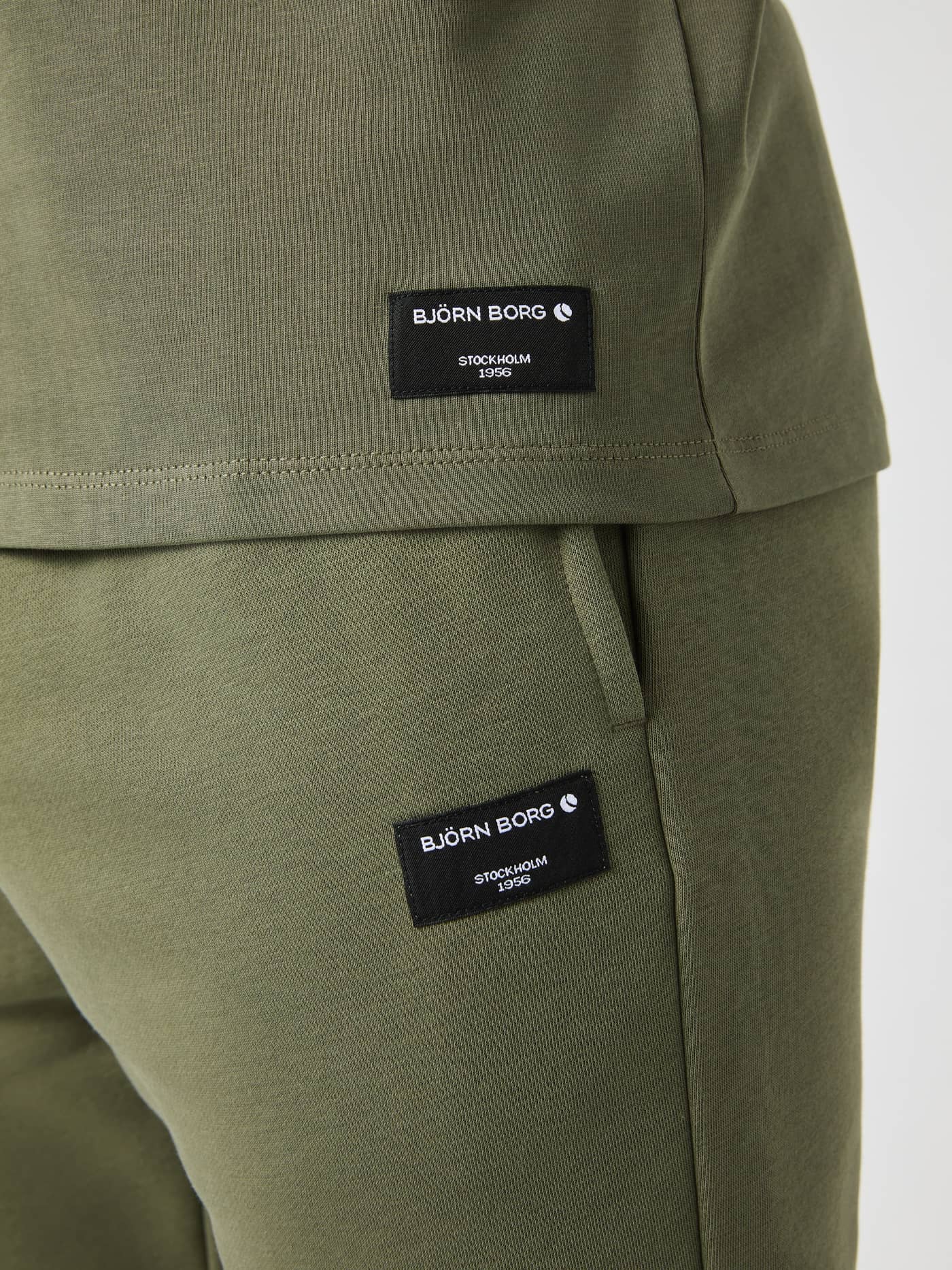 Close-up of the black logo labels on the men's cotton Centre High Neck T-Shirt in Dusty Olive (Green). - Image 5