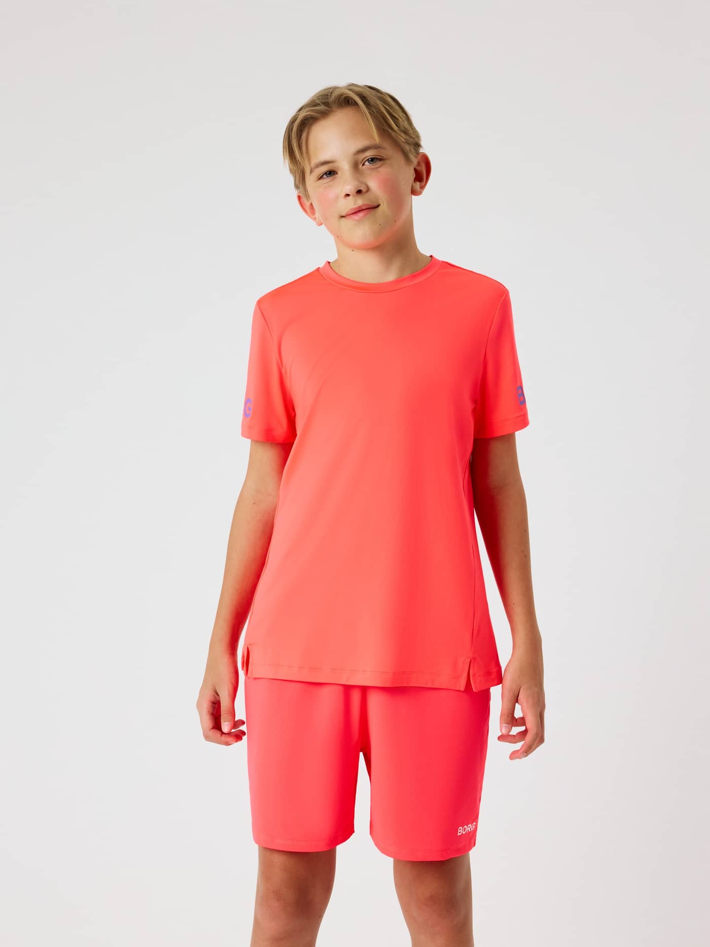 Framifrån på ett barn i Diva Pink (Rosa) Borg T-Shirt för träning med lila logotyper på ärmarna. - Image 4