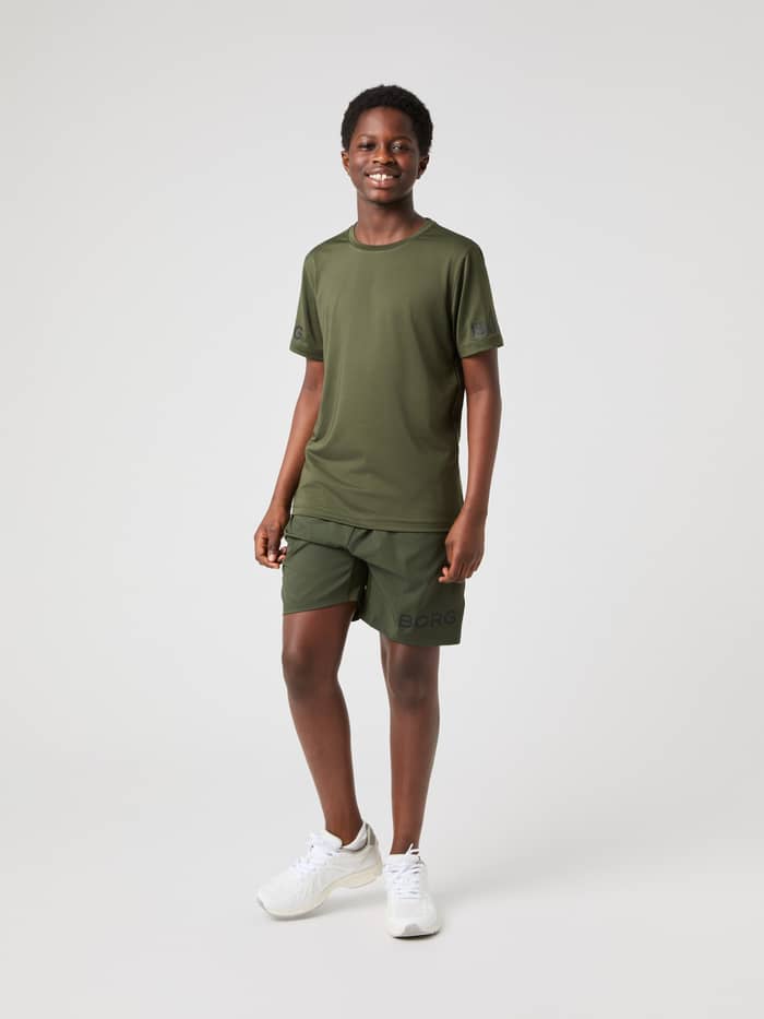 Ganzkörper-Vorderansicht eines Modells im Borg T-Shirt in Forest Night (Grün) mit dunklen Ärmellogos beim Kids-Training. - Image 3