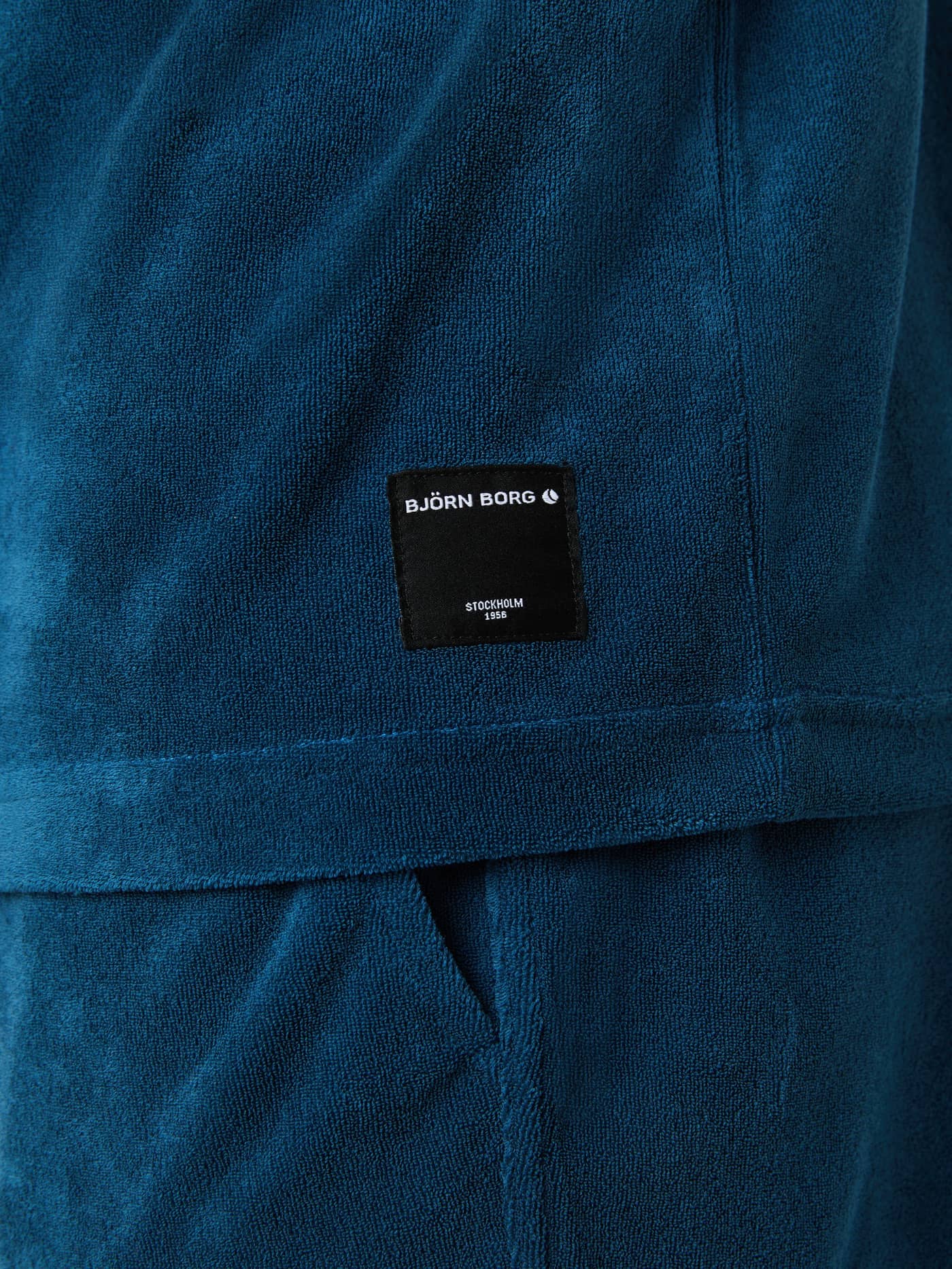 Close-up of the black logo label on the Gibraltar Sea (Blue) Borg Toweling T-Shirt in soft toweling fabric. - Image 4