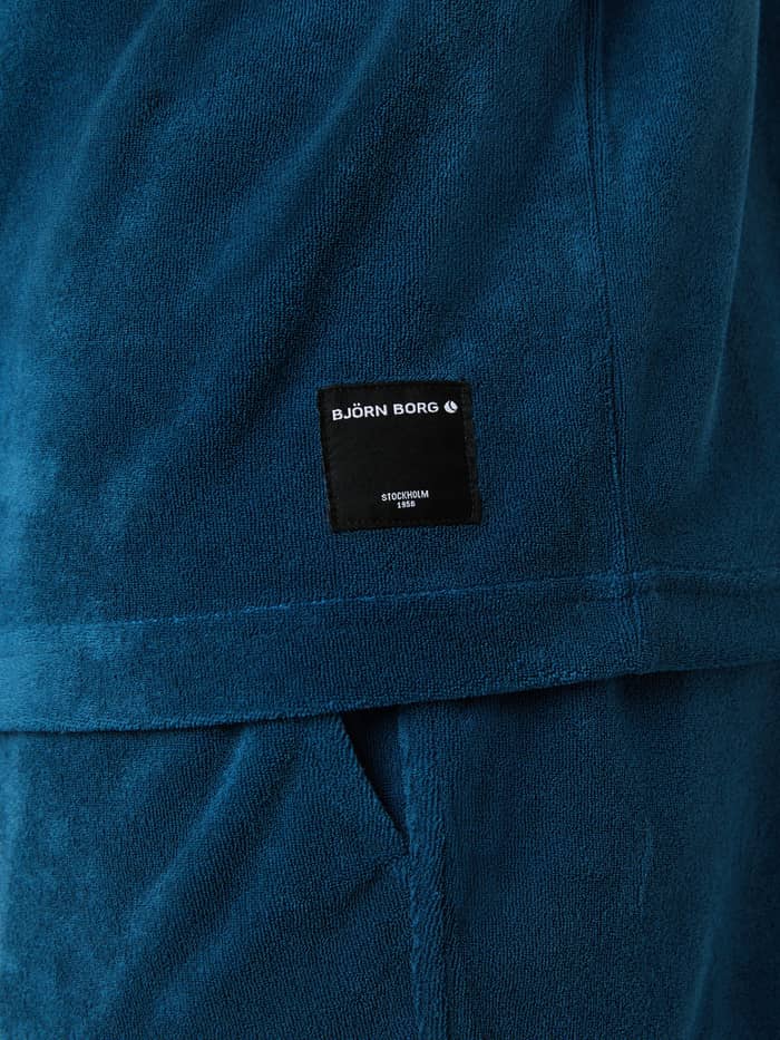 Close-up van het zwarte logolabel op het Borg Toweling T-Shirt in Gibraltar Sea (Blauw) van zachte badstof. - Image 4