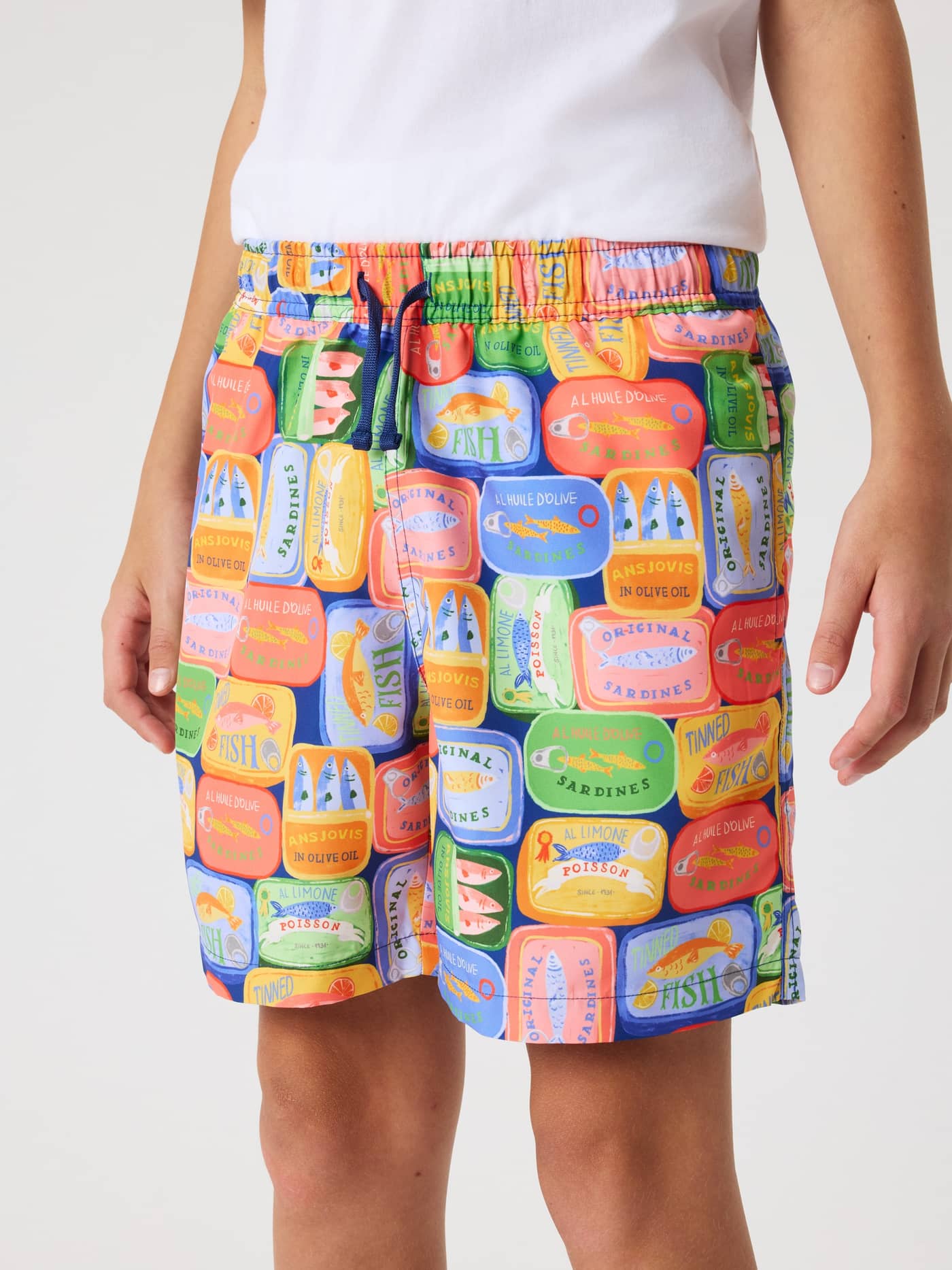 Front view of a model wearing kids' Borg Print Swim Shorts in a vibrant blue, green, and orange sardine print. - Image 2