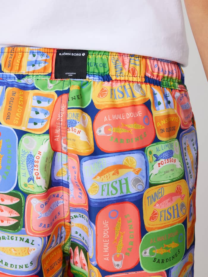 Borg Print Swim Shorts til børn set bagfra i blå, grøn og orange med et livligt sardinprint og sort logo. - Image 4