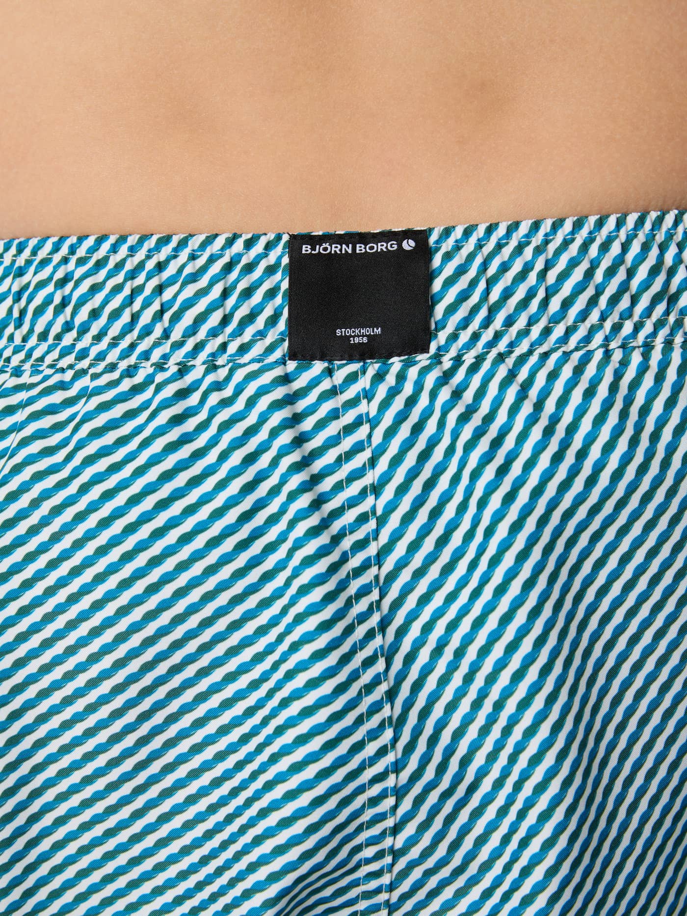 Close-up of the waistband on kids' Borg Print Swim Shorts in Candy Stripe 2 (Blue), featuring a black logo label. - Image 4