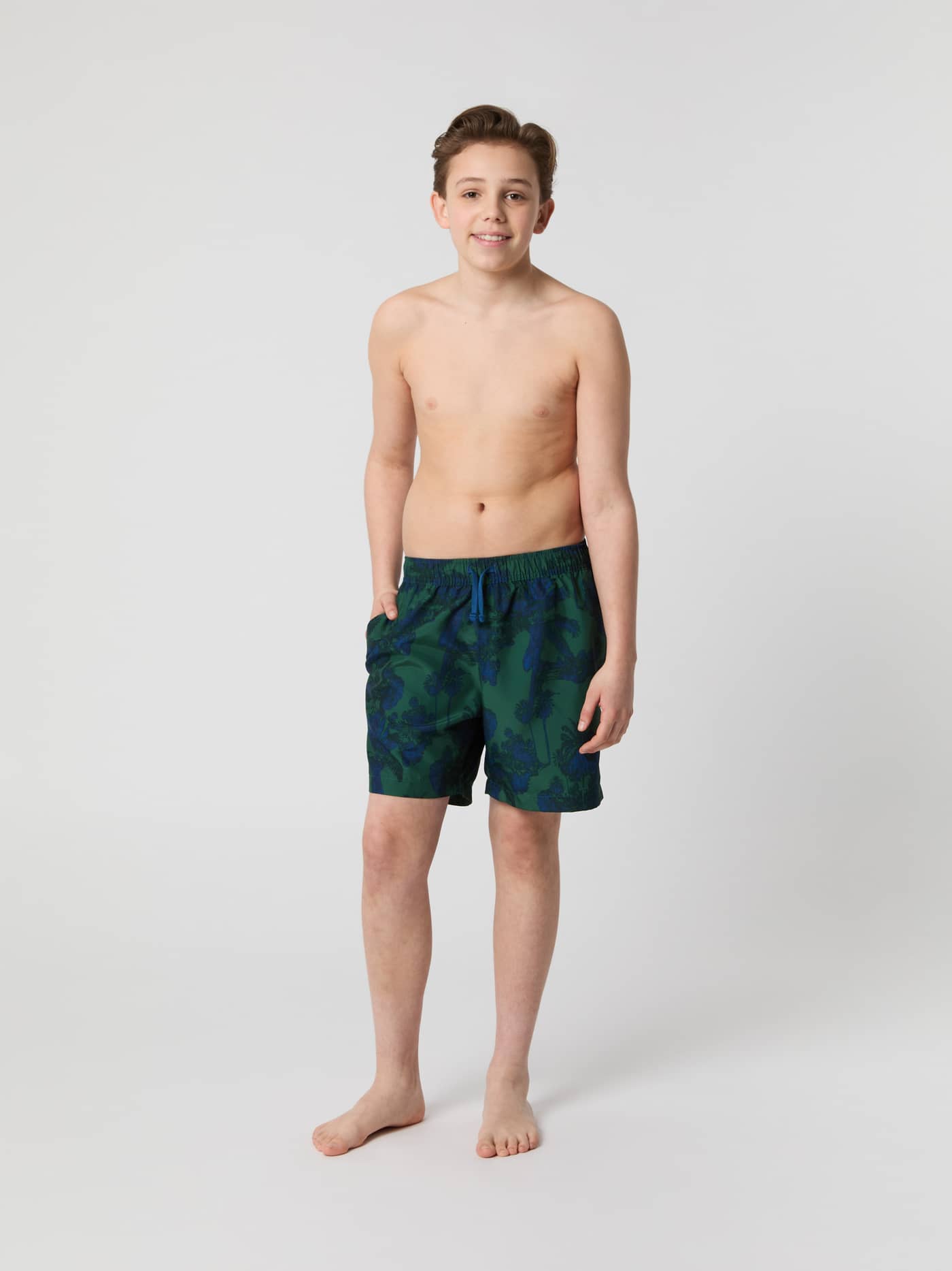 Front view of a kid wearing the Björn Borg Borg Print Swim Shorts in Palm Beach Big 1 (Green) with a tropical pattern. - Image 1