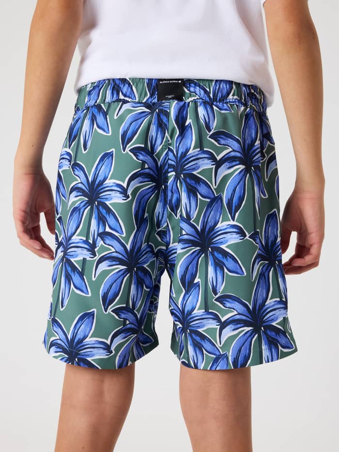 Borg Print Swim Shorts til kids i Palms On Palms 1 (Blå Grøn) med palmetræsprint, set bagfra med sort logomærke. - Image 3