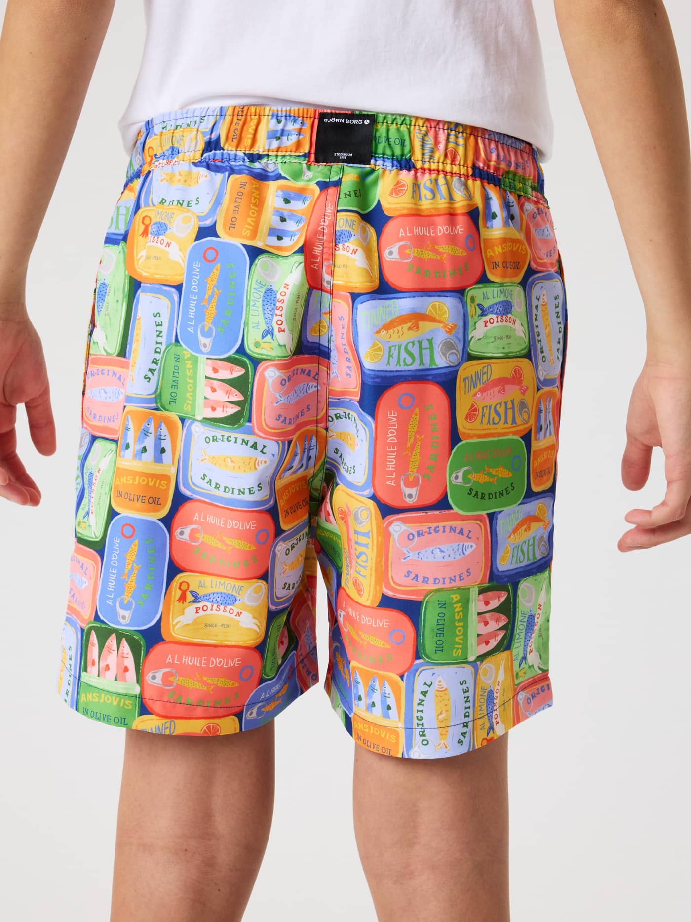 Back view of kids' Borg Print Swim Shorts in a blue, orange, and green sardine print with recycled polyester and black logo. - Image 3