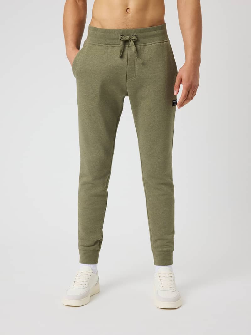 Front view of a model in Centre Tapered Sweatpants in Winter Moss Melange (Green) with a slim fit and black logo.