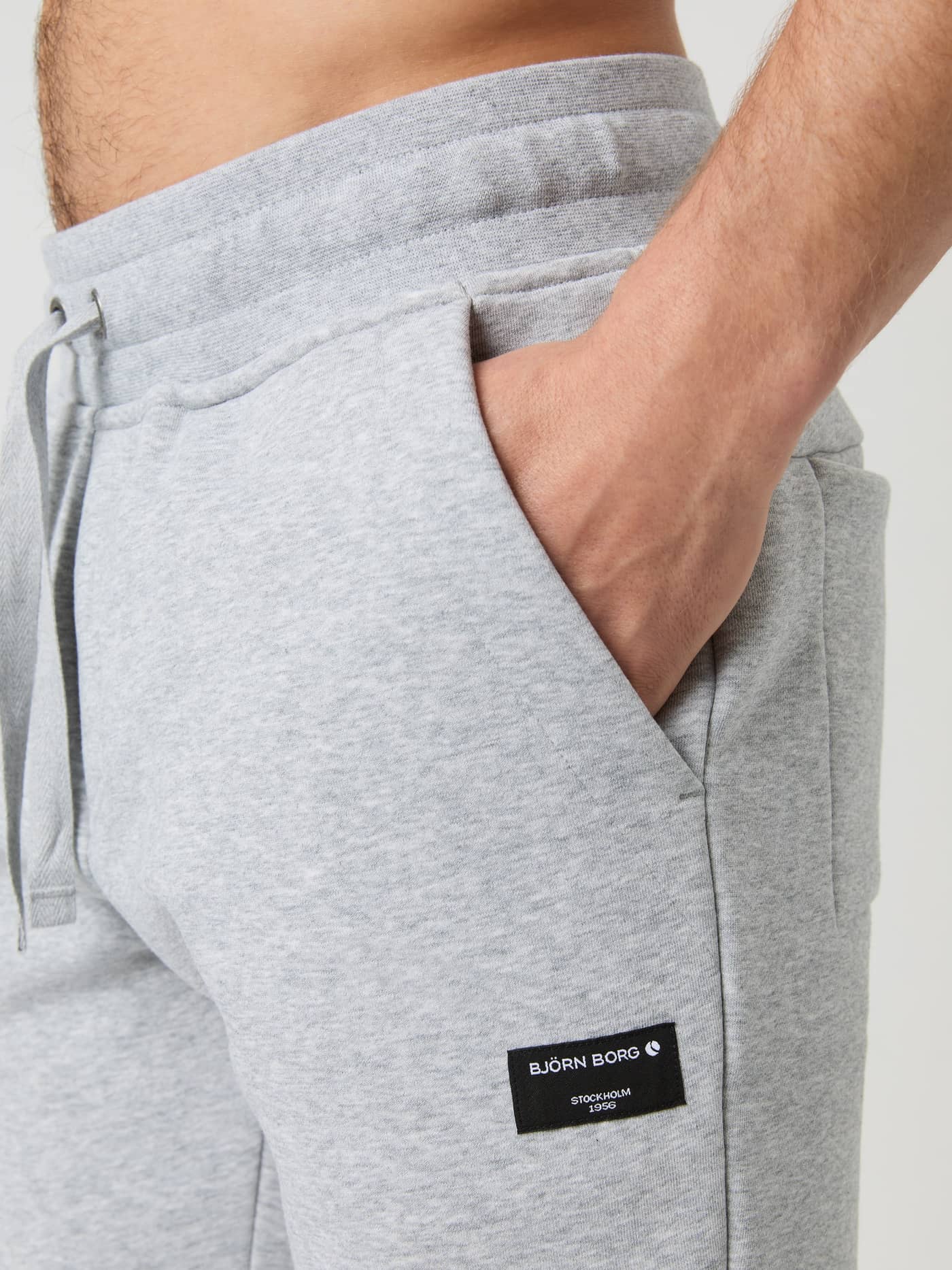 Nahaufnahme der Centre Tapered Sweatpants in Light Grey Melange (Grau) mit Seitentasche, Bund und schwarzem Logo. - Image 4