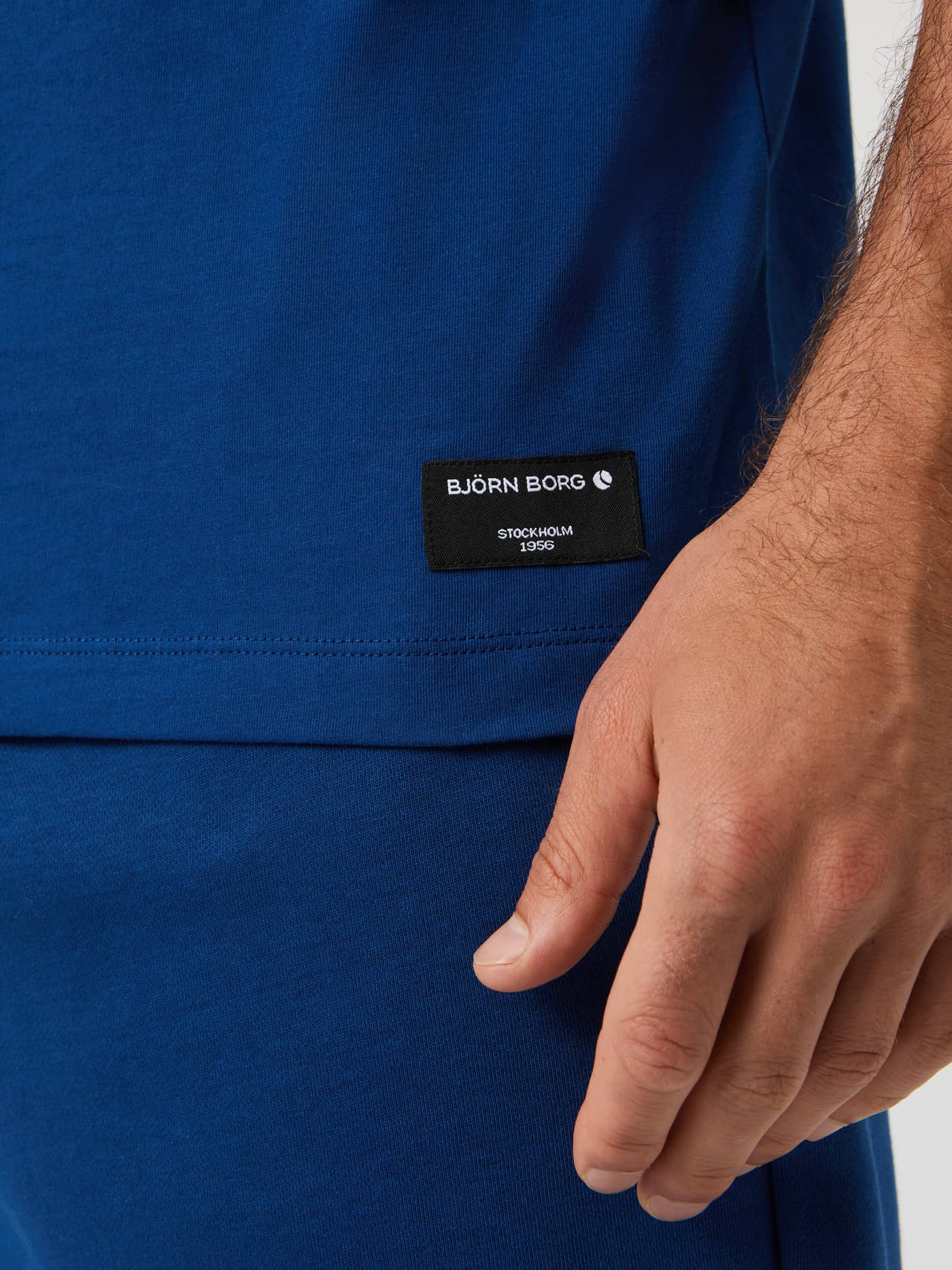 Detail shot of the Björn Borg Centre T-Shirt in estate blue, showing the black brand label on the bottom hem. - Image 4