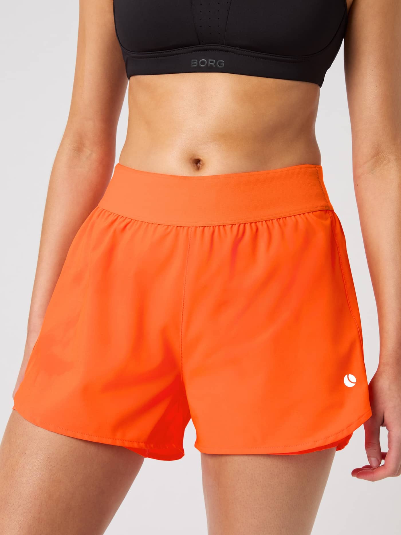 Front close-up of a woman wearing the Björn Borg Ace 2 in 1 Shorts in Shocking Orange. - Image 2