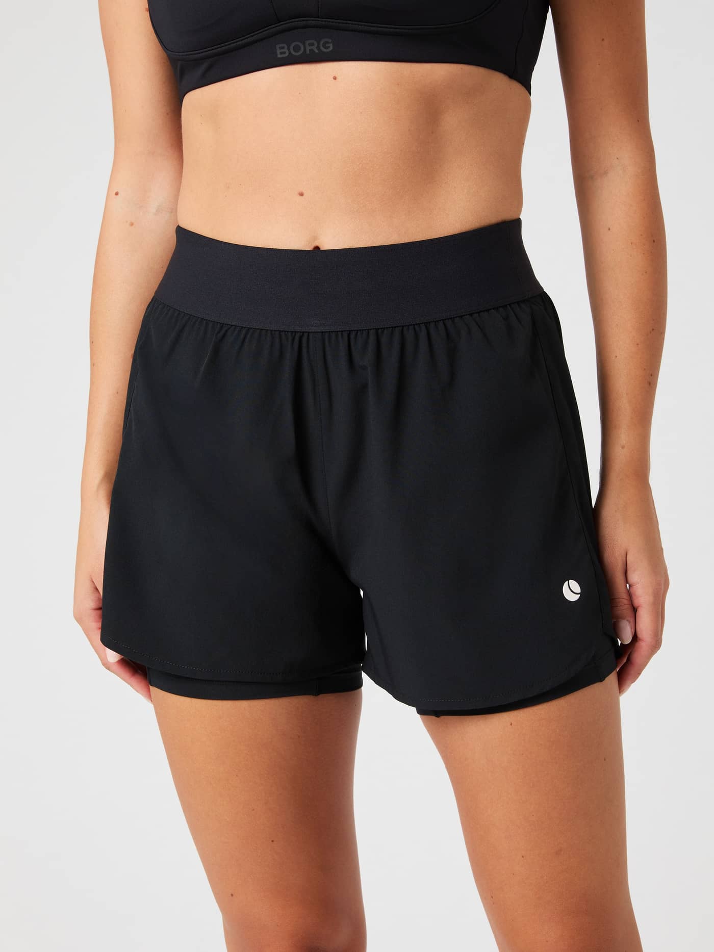 Front view of a woman wearing the black Björn Borg Ace 2 in 1 Shorts, showing the wide elastic waistband and inner shorts. - Image 2