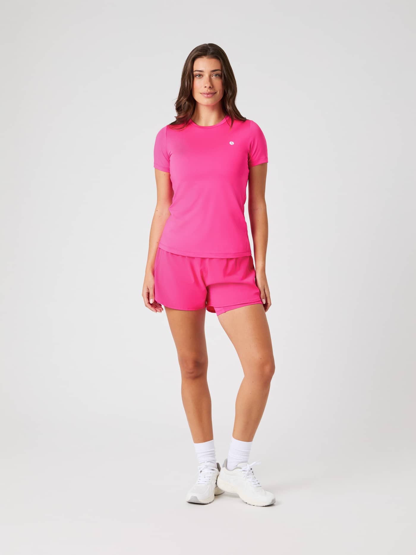 Front view of a woman in a full body shot, wearing the Björn Borg Ace 2-in-1 Shorts in Pink Glo and a matching top. - Image 1