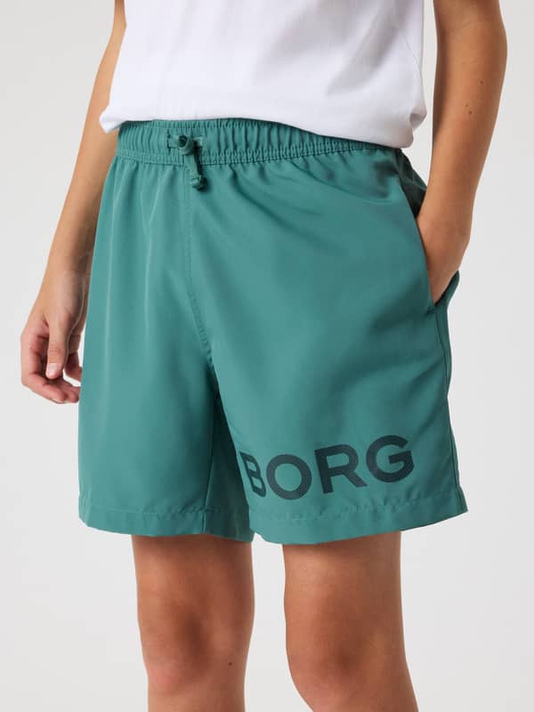 Hurtigtørrende Borg Swim Shorts til børn i Blue Spruce (Grøn) set forfra med et stort sort logo på benet.