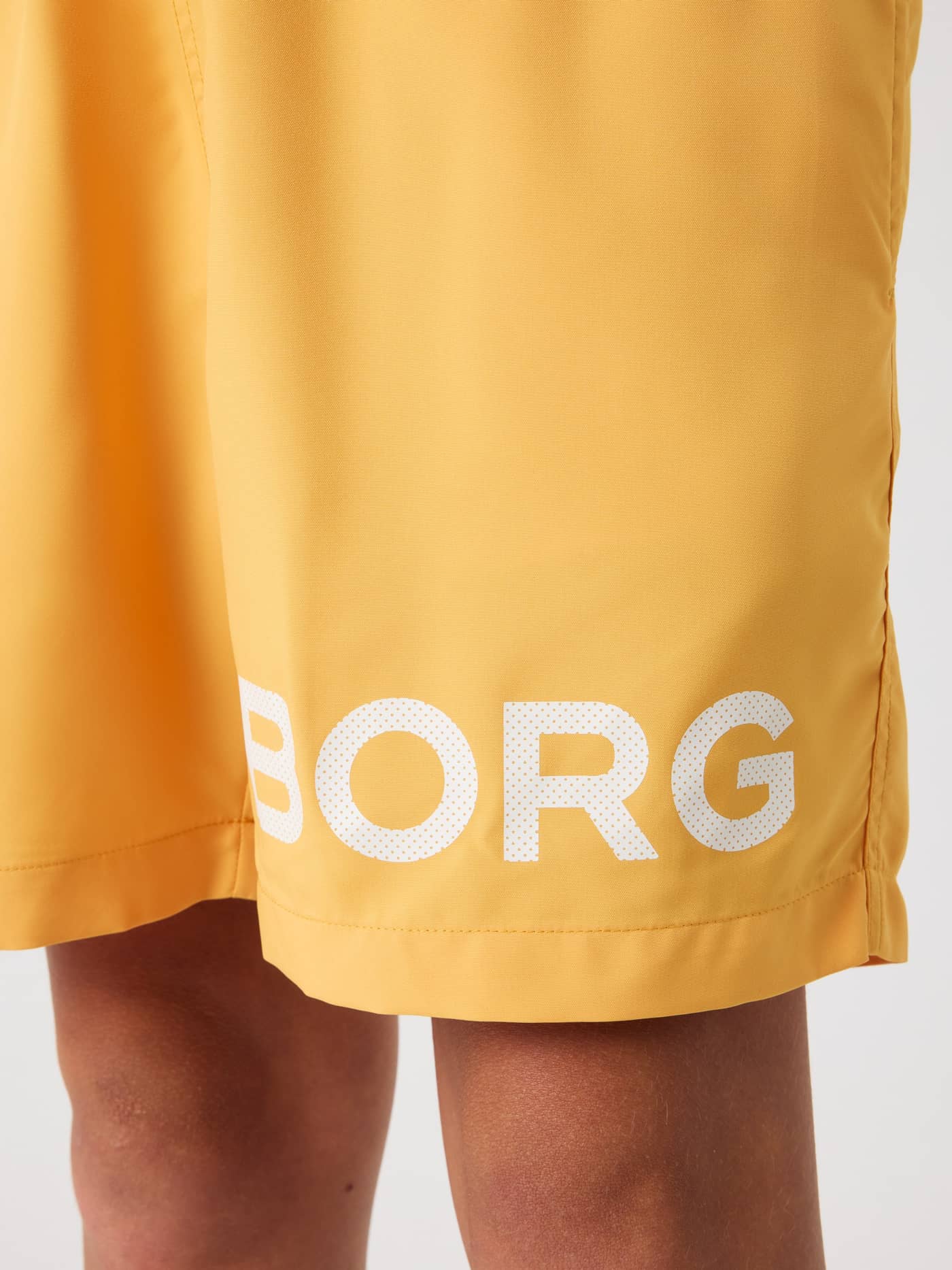 Borg Swim Shorts i Marigold (Gul) til børn set tæt på med et stort hvidt logoprint på benet. - Image 5