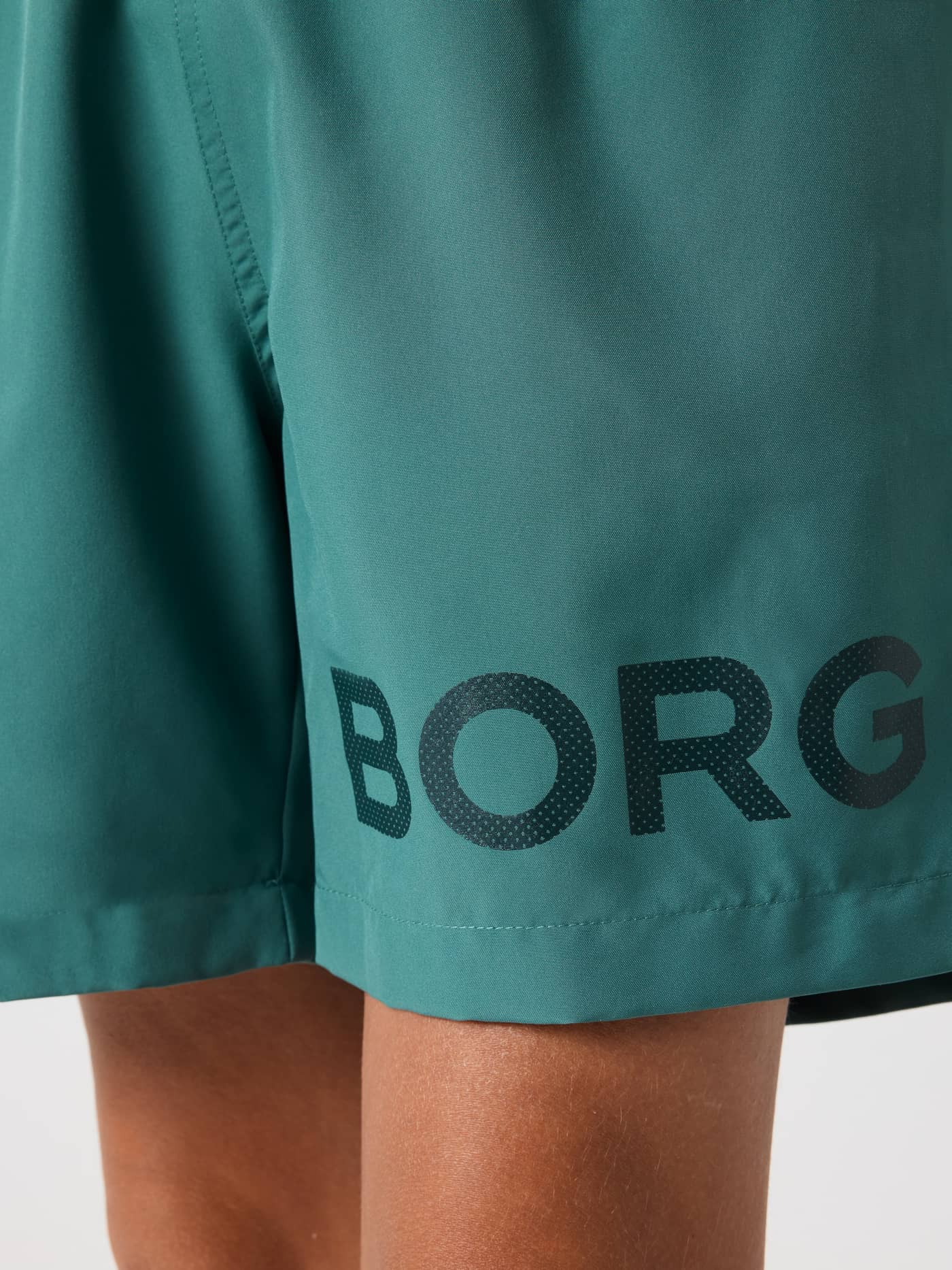 Close-up of the Borg Swim Shorts for kids in Blue Spruce (Green) showing the black logo. - Image 5