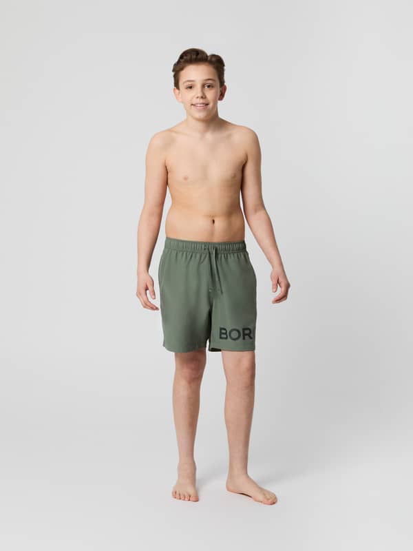 Borg Swim Shorts til kids i Agave Green (Grøn) med almindelig pasform og sort logo, set forfra i fuld figur.
