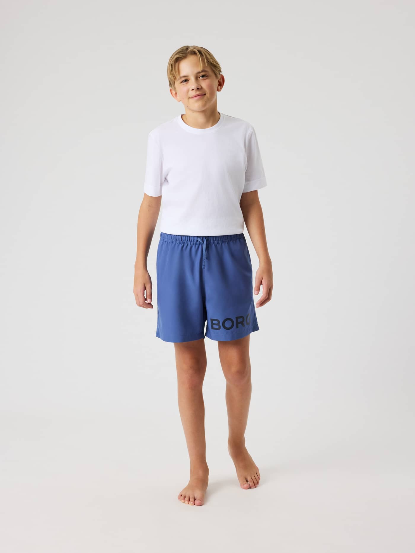 Front view of a boy wearing the kids' Borg Swim Shorts in Coastal Fjord (Blue) with a regular fit and a black logo. - Image 3