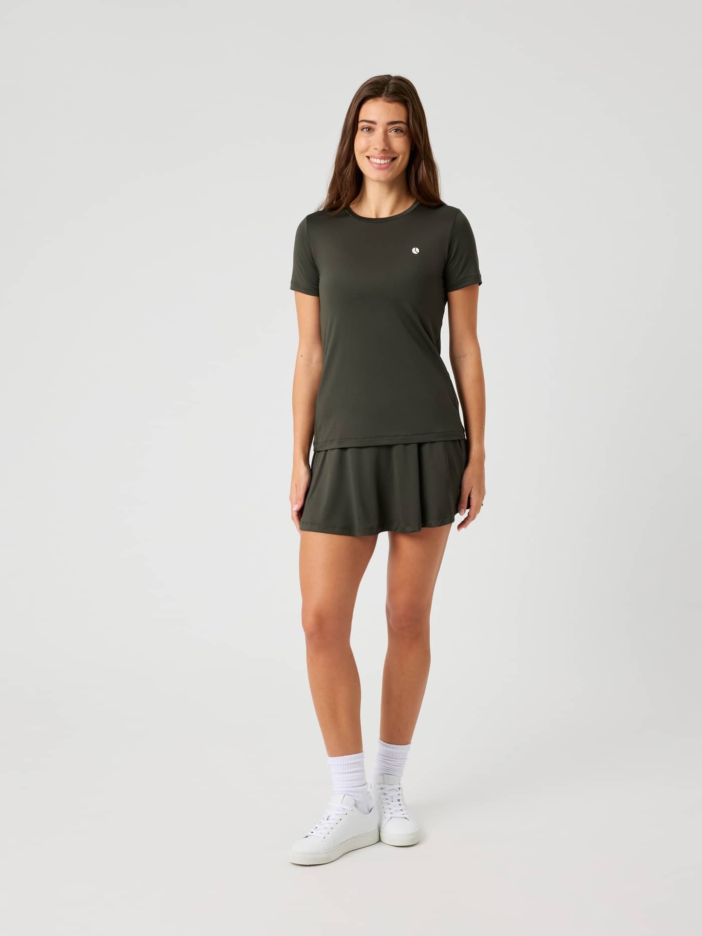 Full-length front view of a woman wearing the Björn Borg Ace Slim T-Shirt in peat, styled with a matching tennis skirt. - Image 3